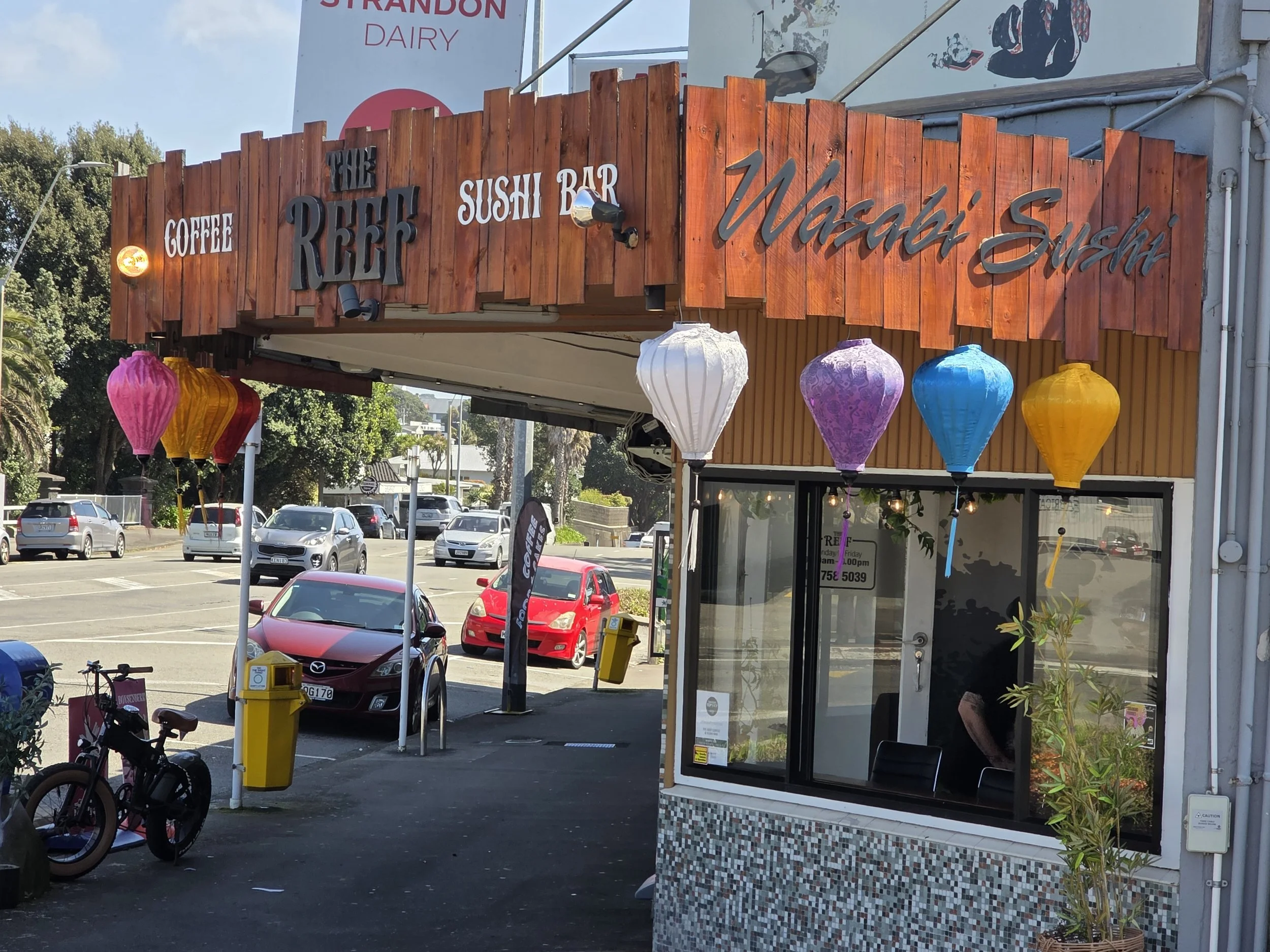 'Reef Sushi Bar' decorated with colorful paper lanterns at the intersection of E Devon St and Nobs Line in Strandon, New Zealand.