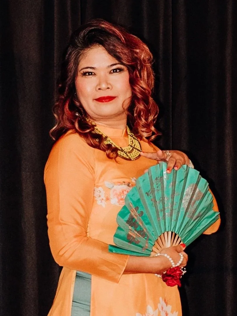 Lyly modeling traditional Vietnamese dress, in orange with teal accents and a fan.