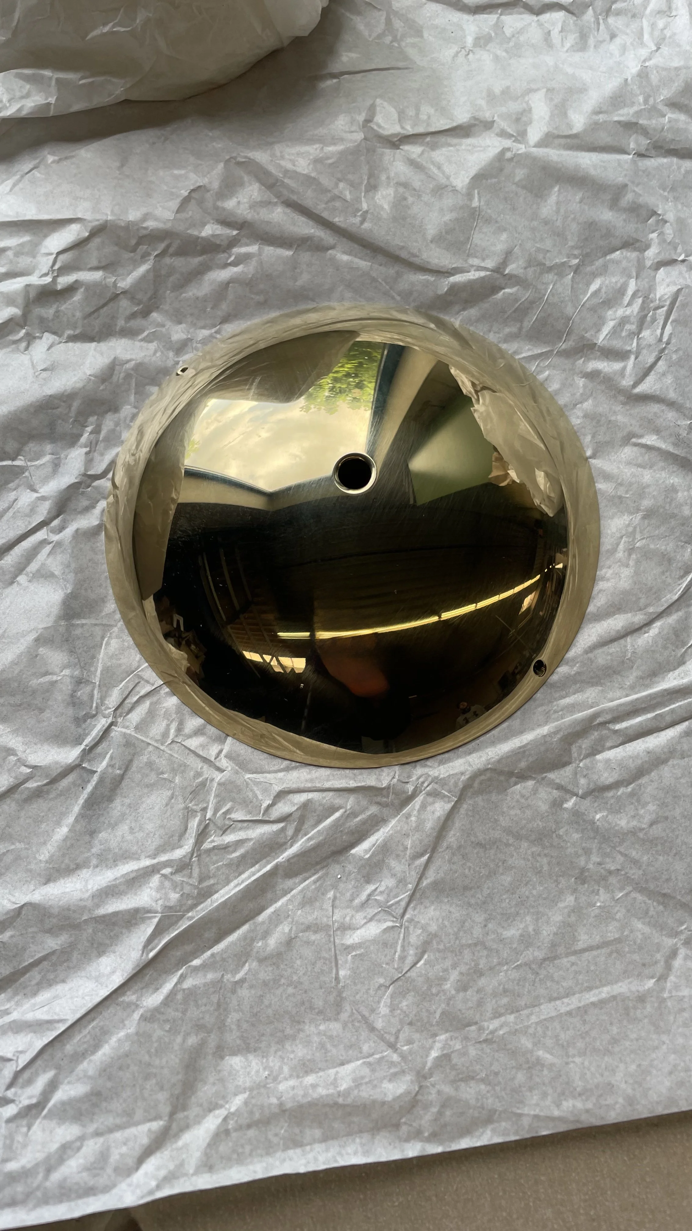 A chrome hub cap with a reflective surface, placed on white wrapping paper.