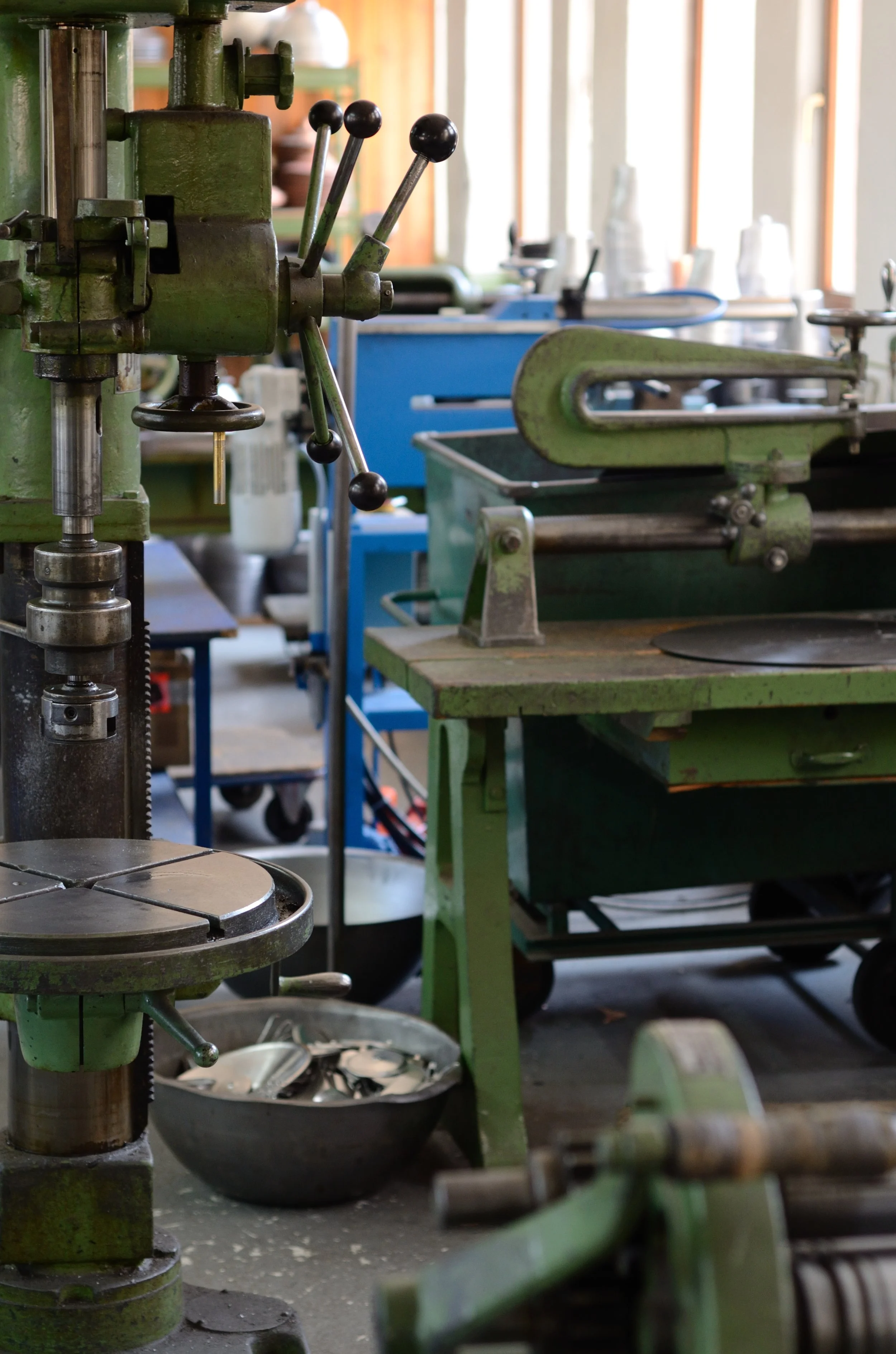 Industrial workshop with green metal machinery, workbenches, and bowls filled with tools or metal parts.