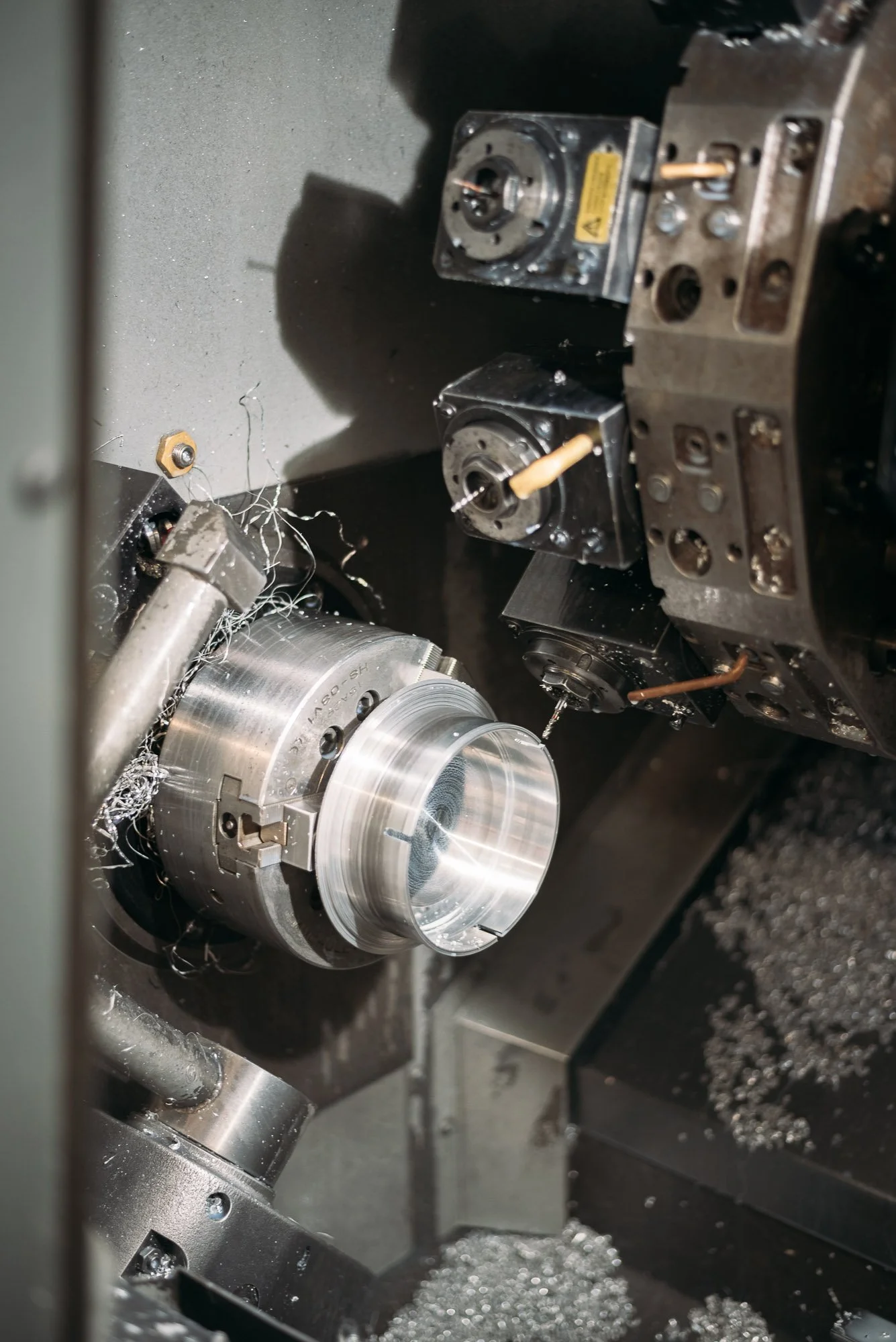 Close-up of metal lathe machine with shiny, nearly finished metal piece being machined, surrounded by metallic shavings and machine components.