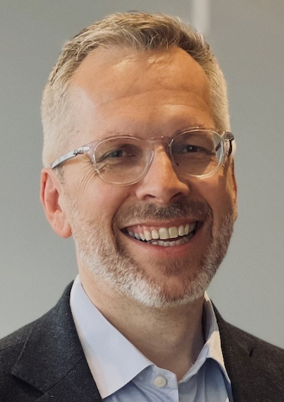 Portrett av en mann med kort, lyst hår, briller, skjegg og smoking, smilende.