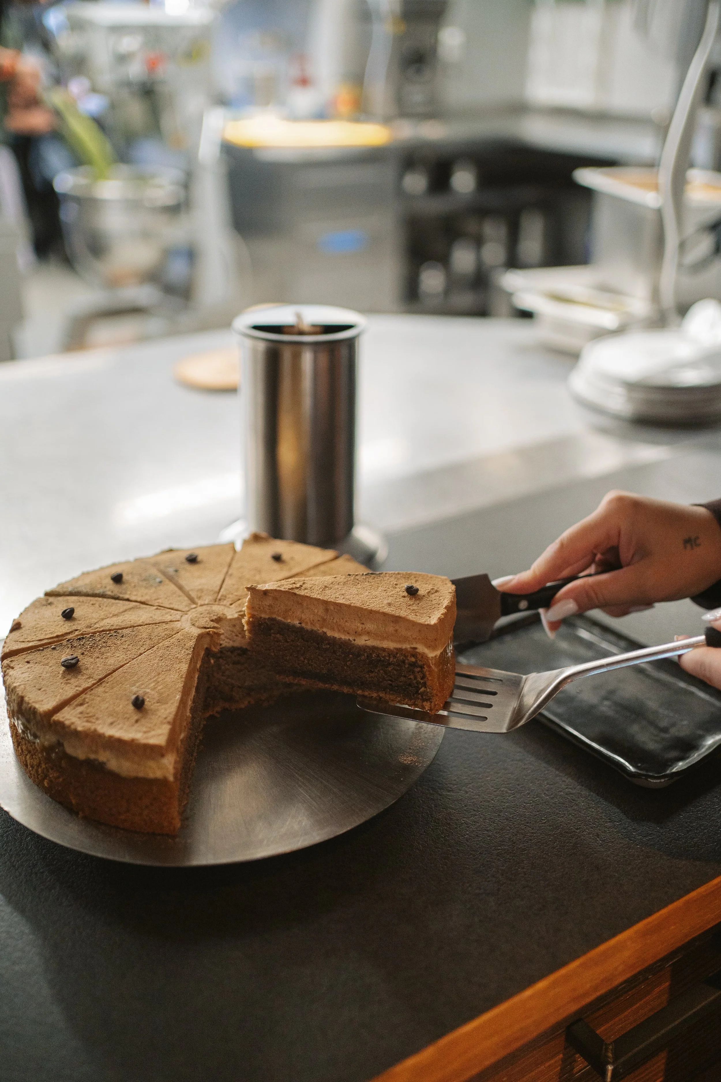 Kuchen auf einem Tisch, jemand schneidet ein Stück ab, im Hintergrund eine Kaffeetasse