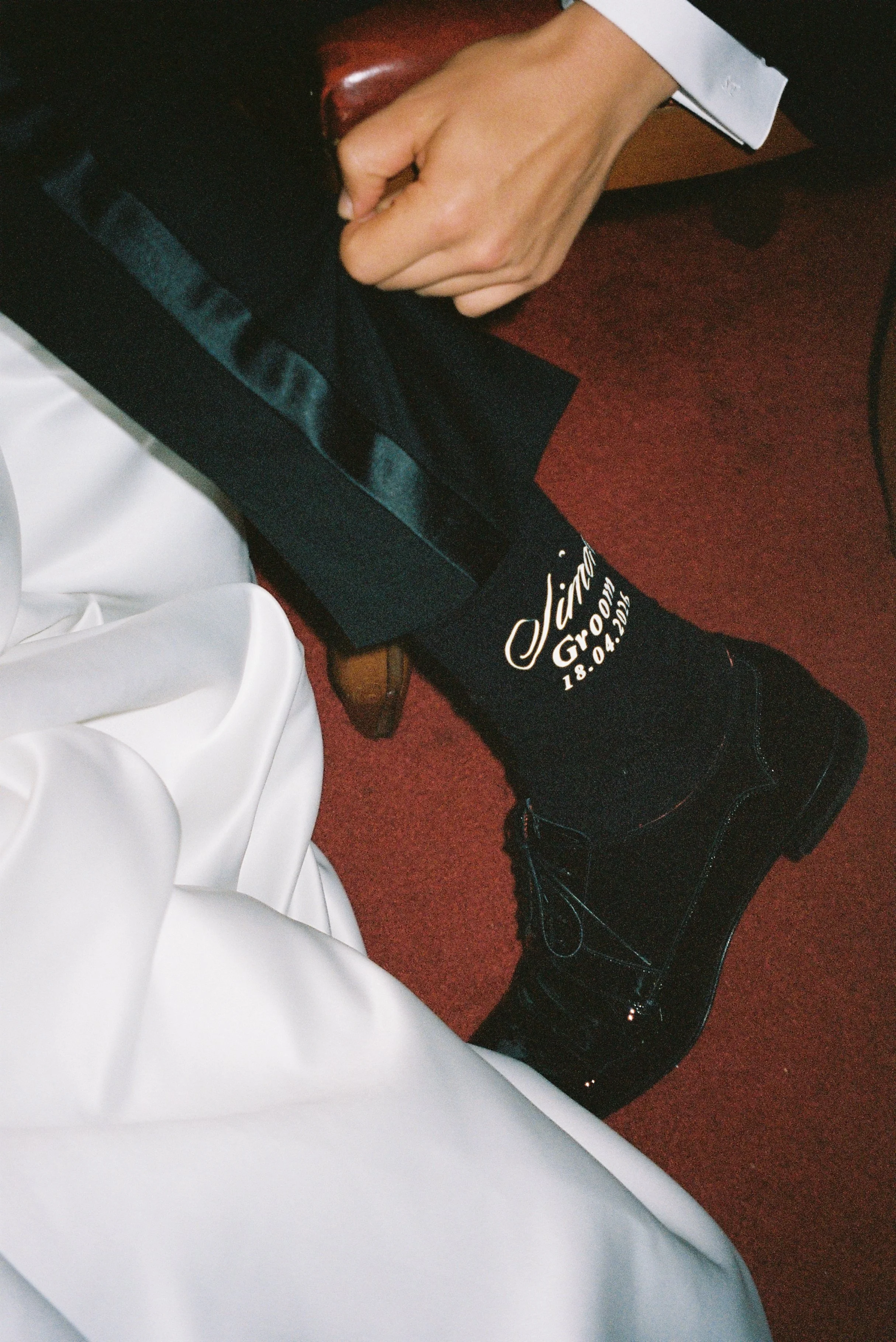A person sitting on a chair, wearing black shoes and black socks with text that reads "Groom" and the date of the wedding.