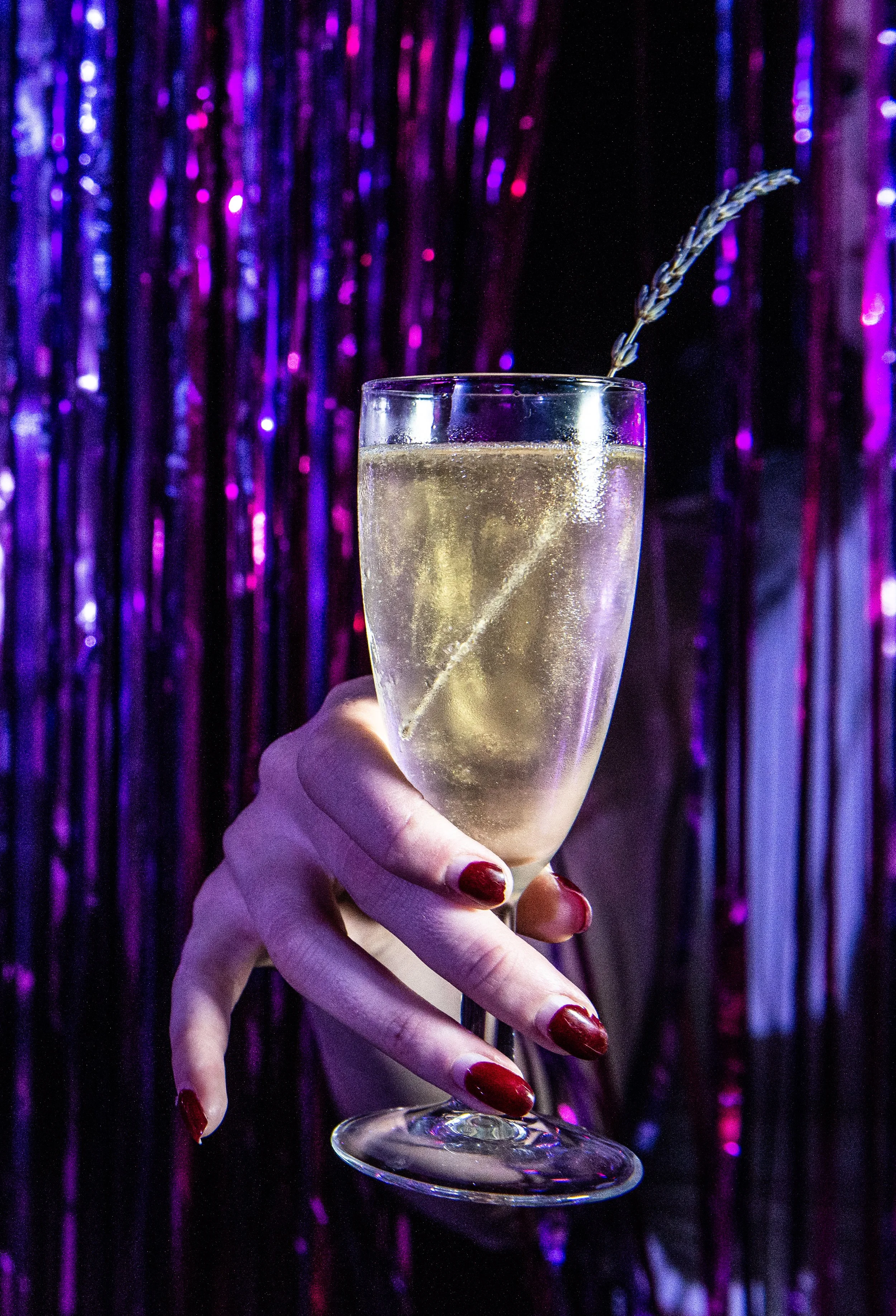 A hand with red painted nails holding a glass of champagne with a purple receipt in the background.