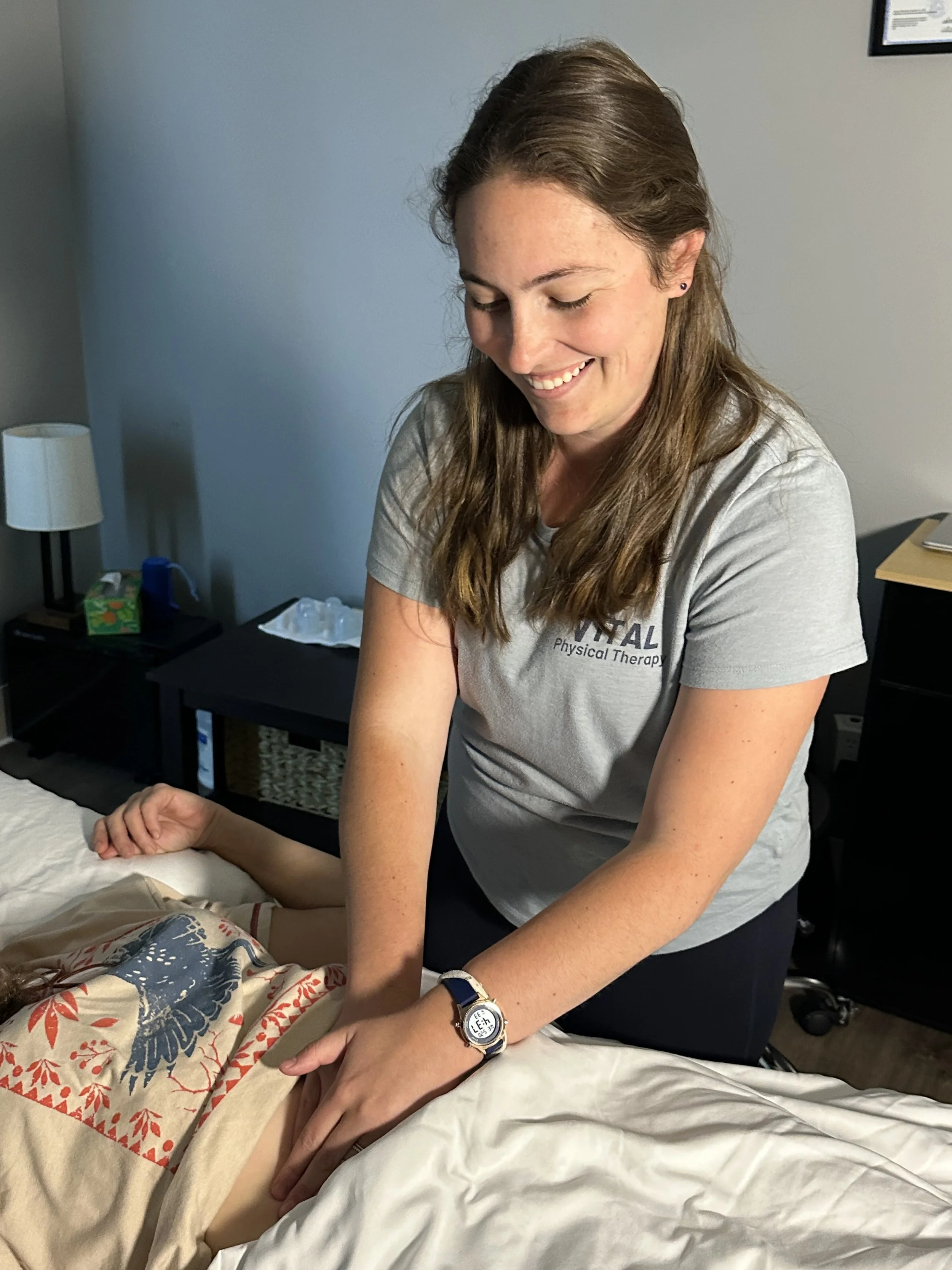 A woman in medical scrubs giving a massage to a patient lying on a bed in a clinical setting.