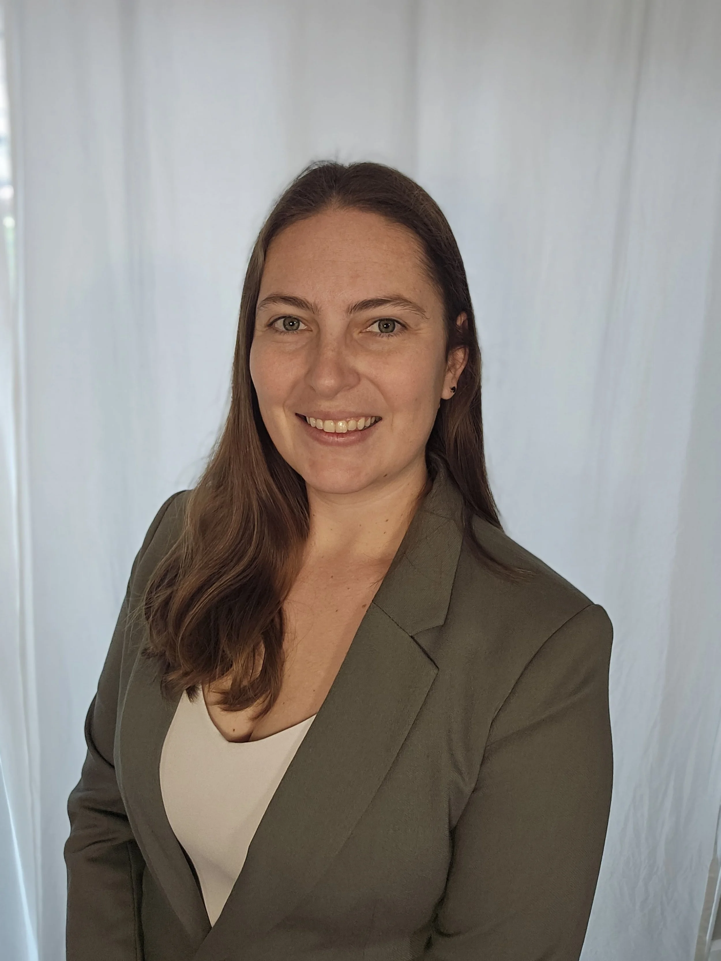 A St. Charles, Missouri, woman with long brown hair, wearing a brown blazer and white top, smiling at the camera, standing against a light background.
