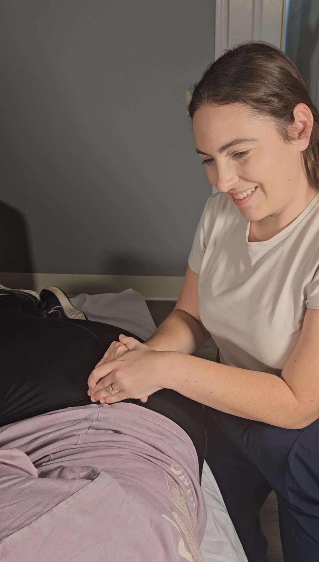 A woman performing a medical examination on a person's abdomen while smiling. Pelvic floor physical therapy. pregnancy, postpartum, and women's healthcare