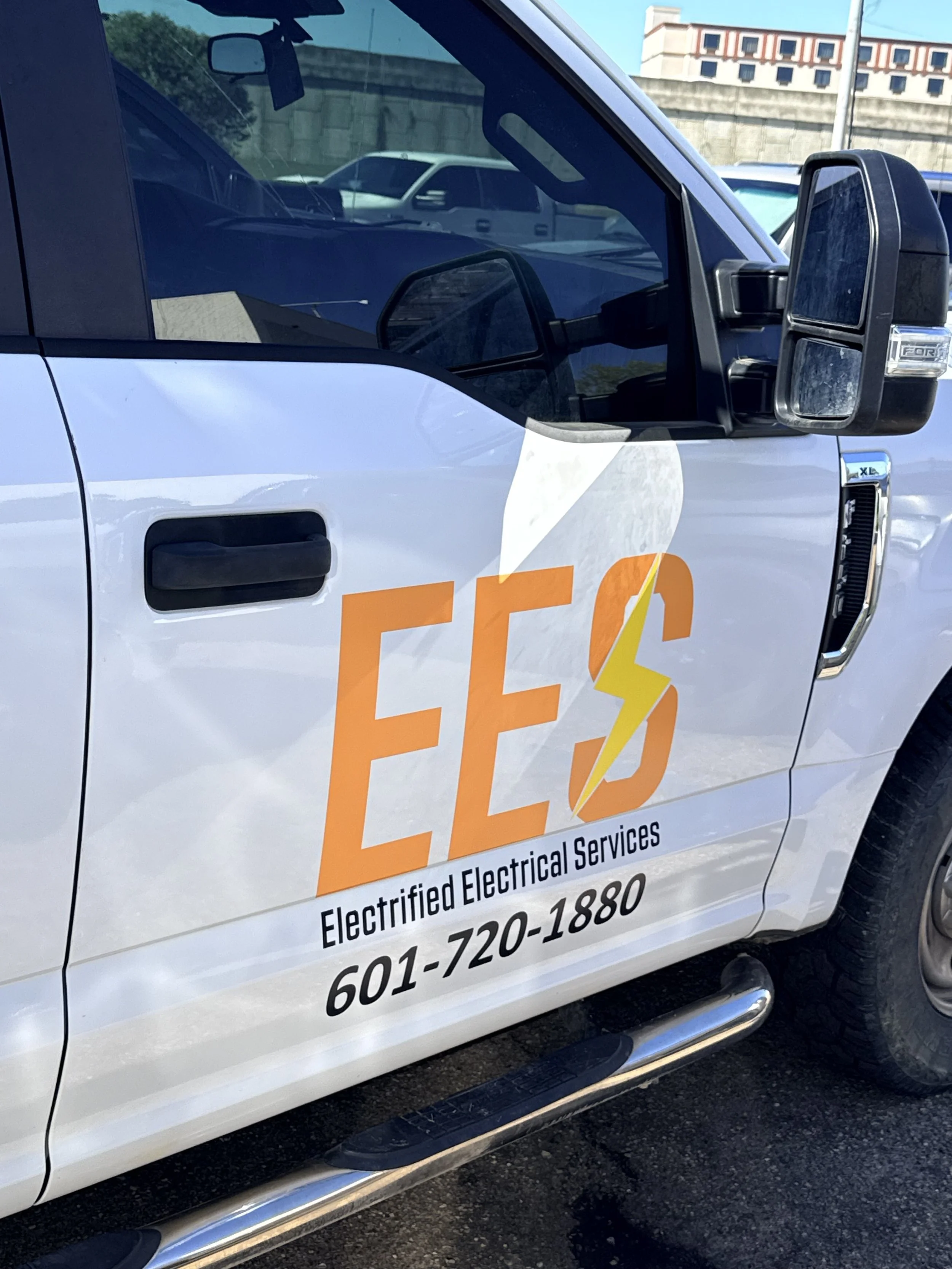 A white work truck with a logo for Electroed Electrical Services, featuring the letters 'EES' with a yellow lightning bolt. The truck also displays a phone number, 601-720-1880.