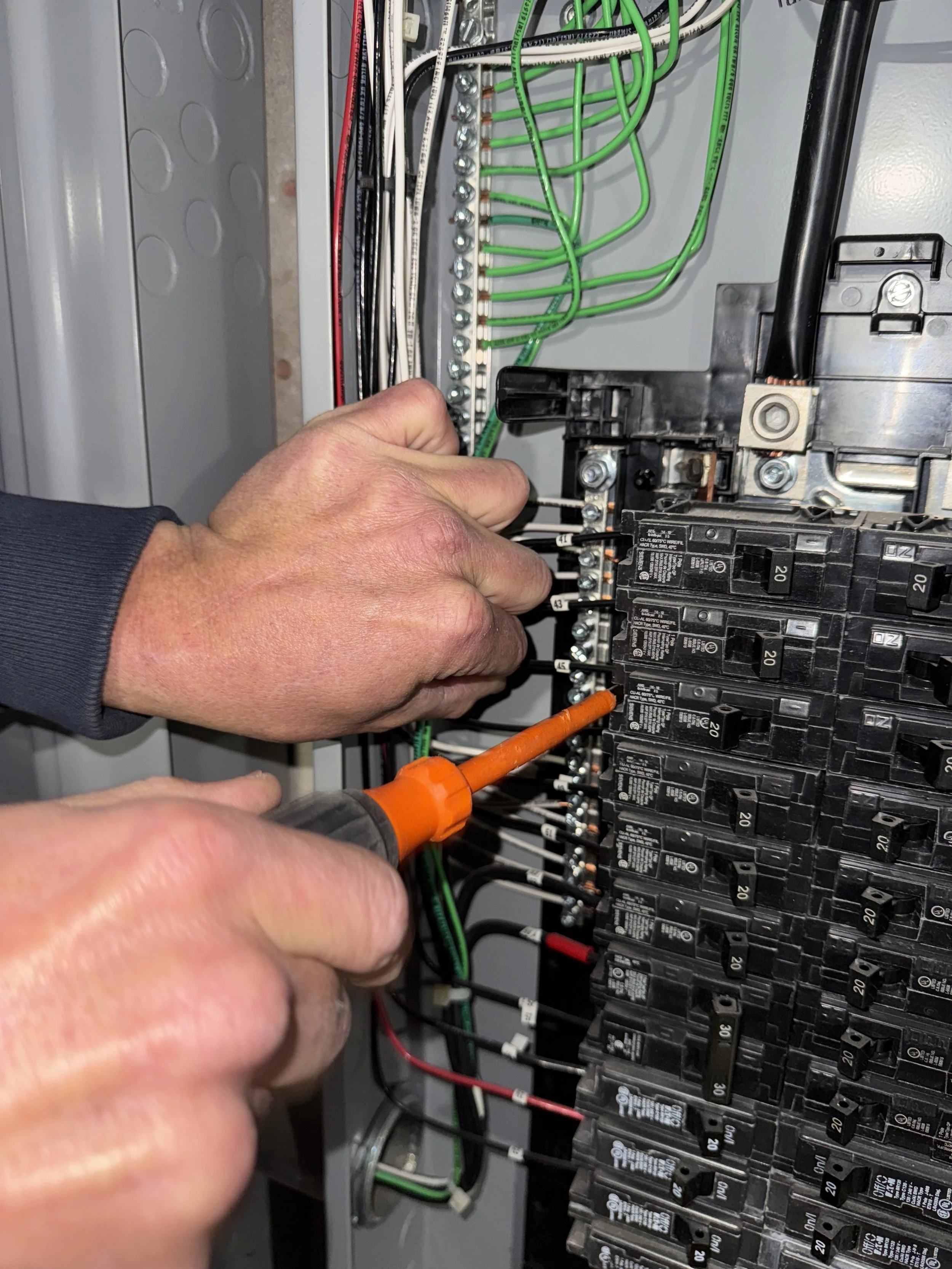 A person working on an electrical breaker panel, using a screwdriver and screwdriver to adjust wiring and circuit breakers.