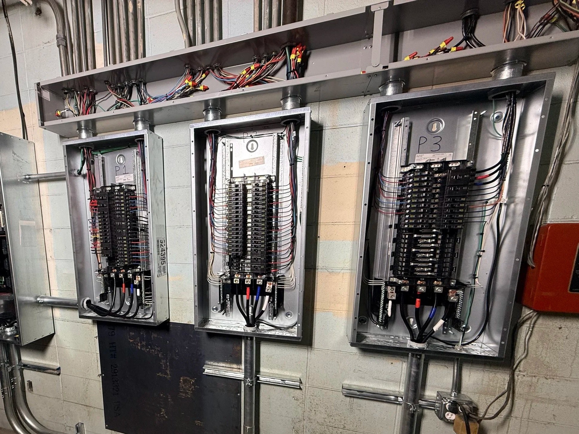 Electrical panels with circuit breakers and wiring mounted on a concrete wall.