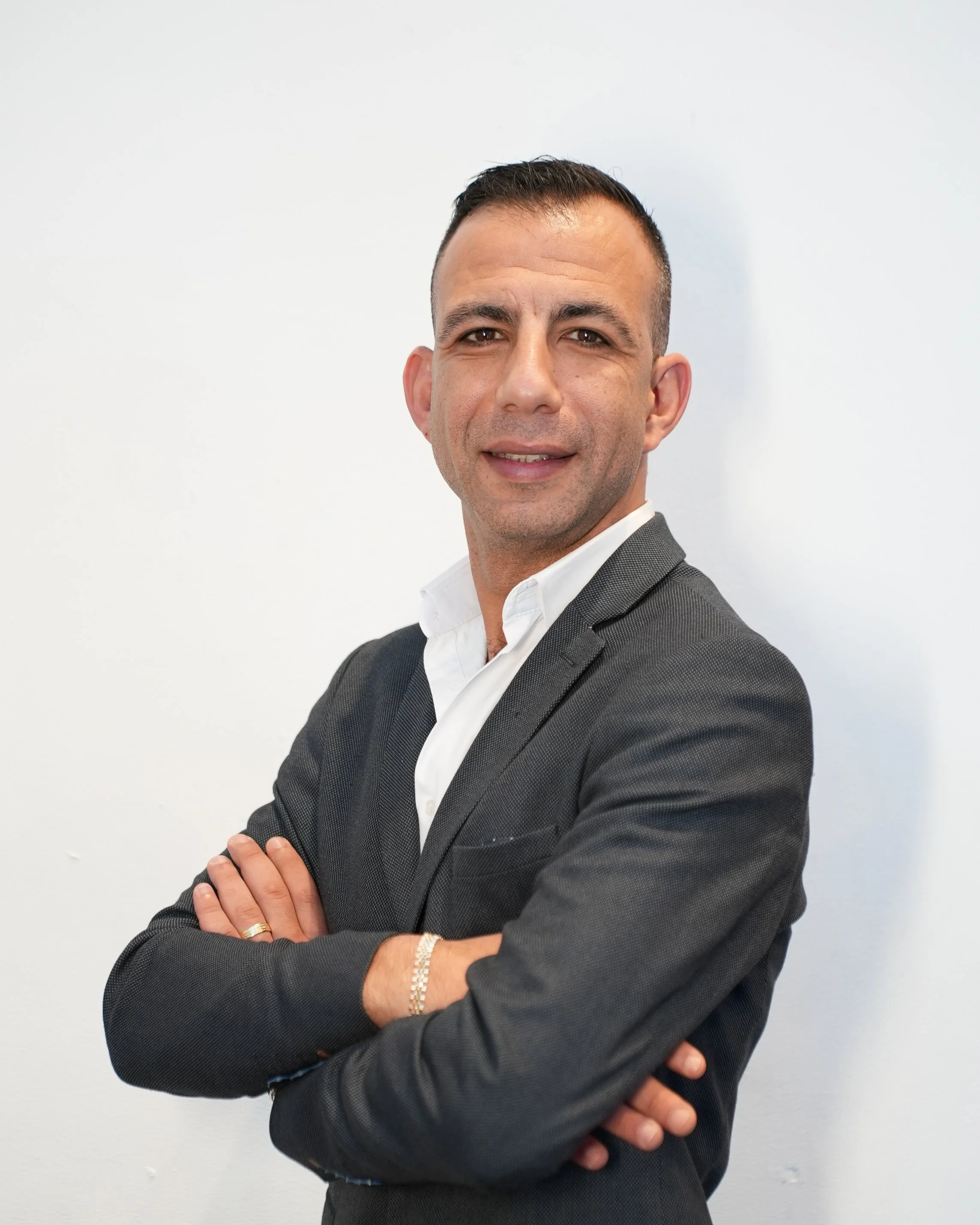 Professional man in suit with arms crossed, standing against a white background.
