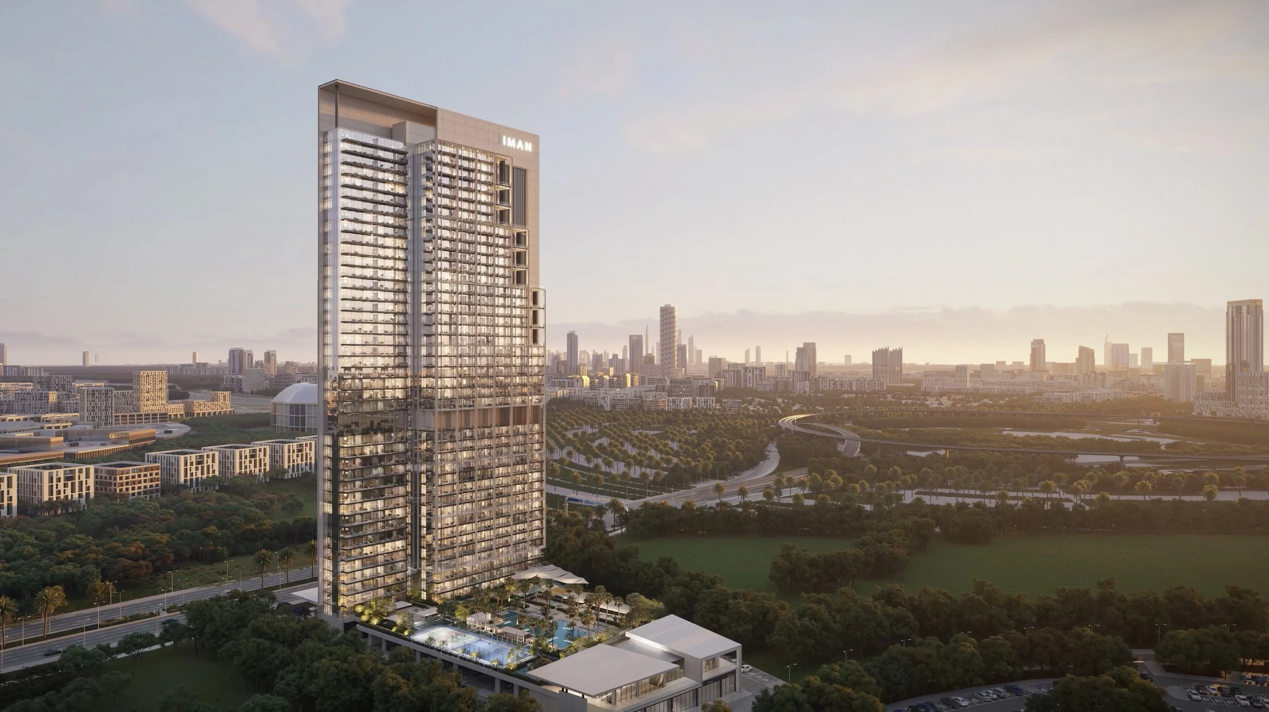 A tall modern skyscraper with glass windows and balconies, with a city skyline in the background during sunset, and a green park with trees in the foreground.