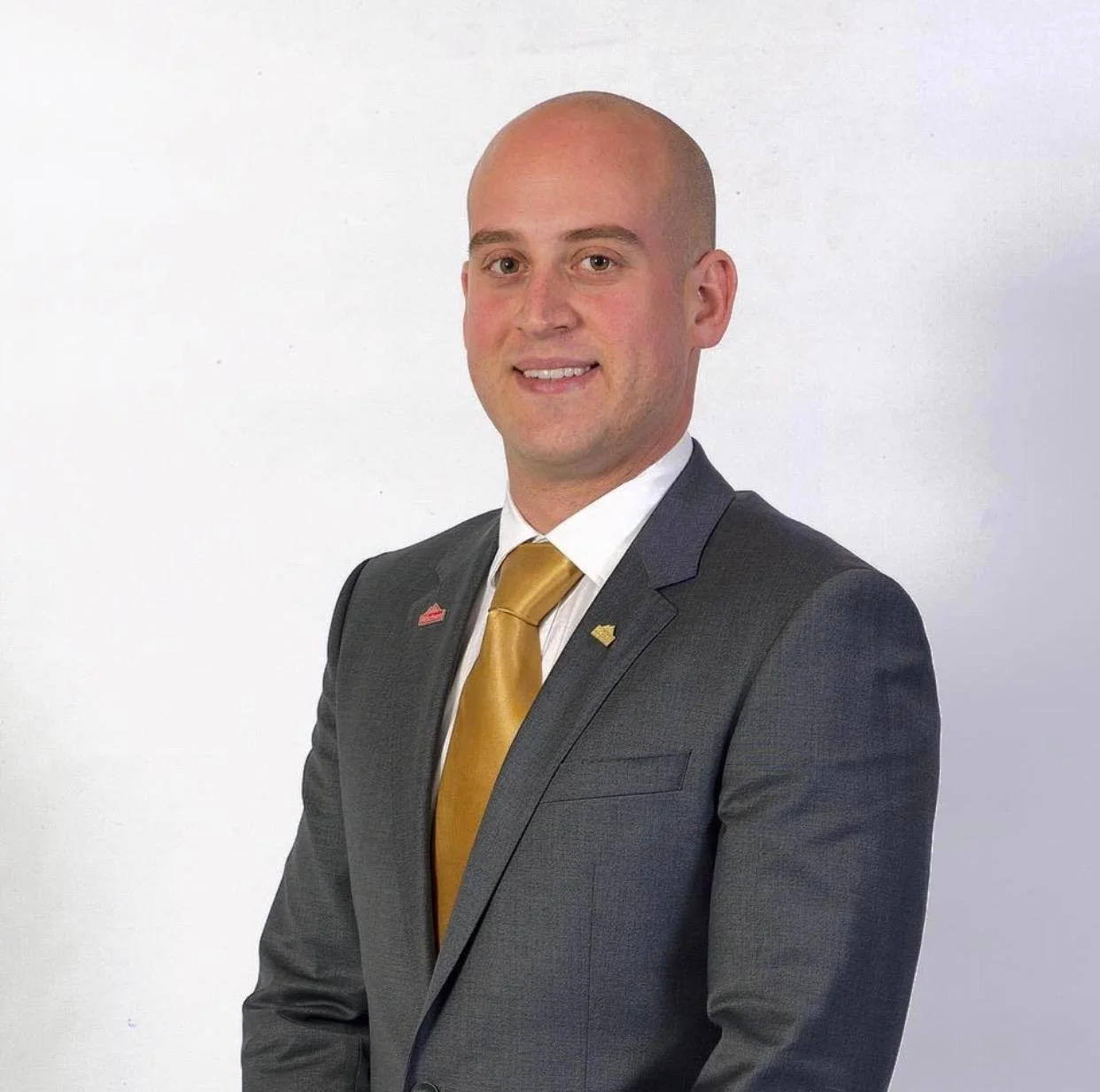 A man in a gray suit and gold tie, standing against a plain white background.