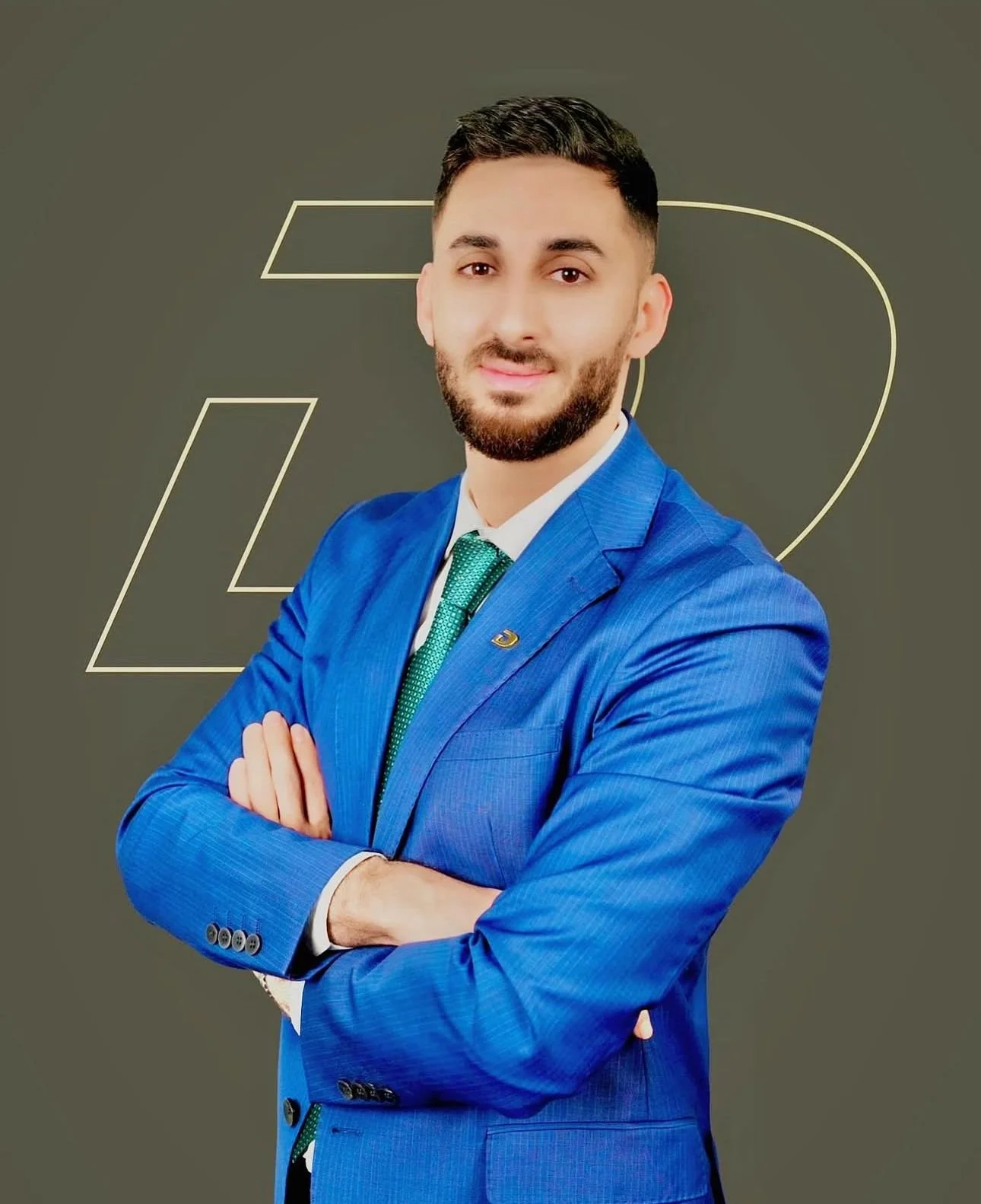 A man in a blue suit and green tie with arms crossed, standing in front of a dark background with geometric designs.