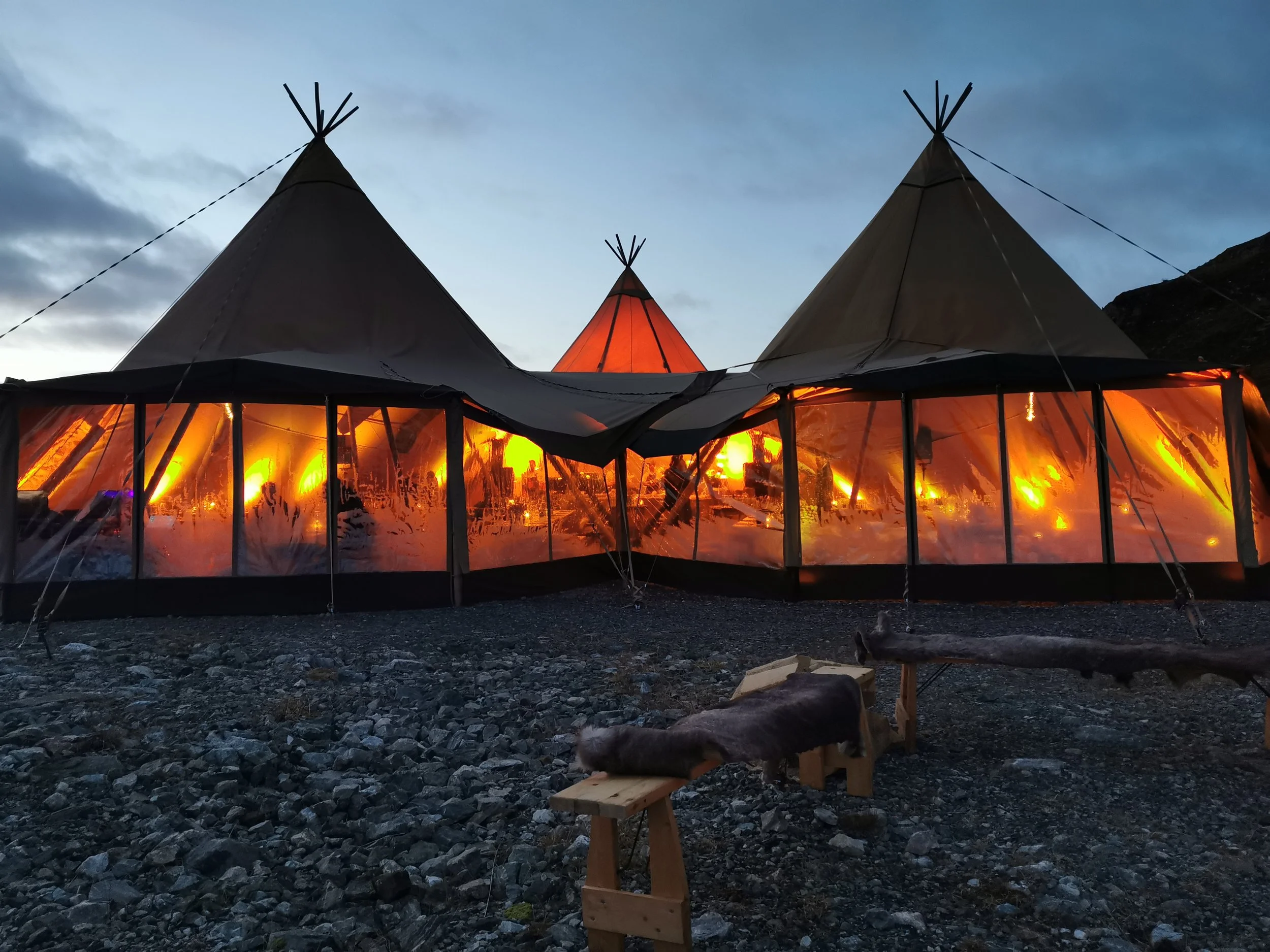 Teppe av telt på fjell, med varme lys innvendig, og steinede bakken foran.