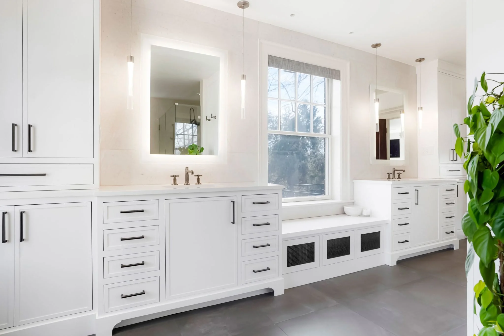 Bright bathroom with white cabinetry, two mirrors with backlit LED lights, and large windows with a view of trees outside.