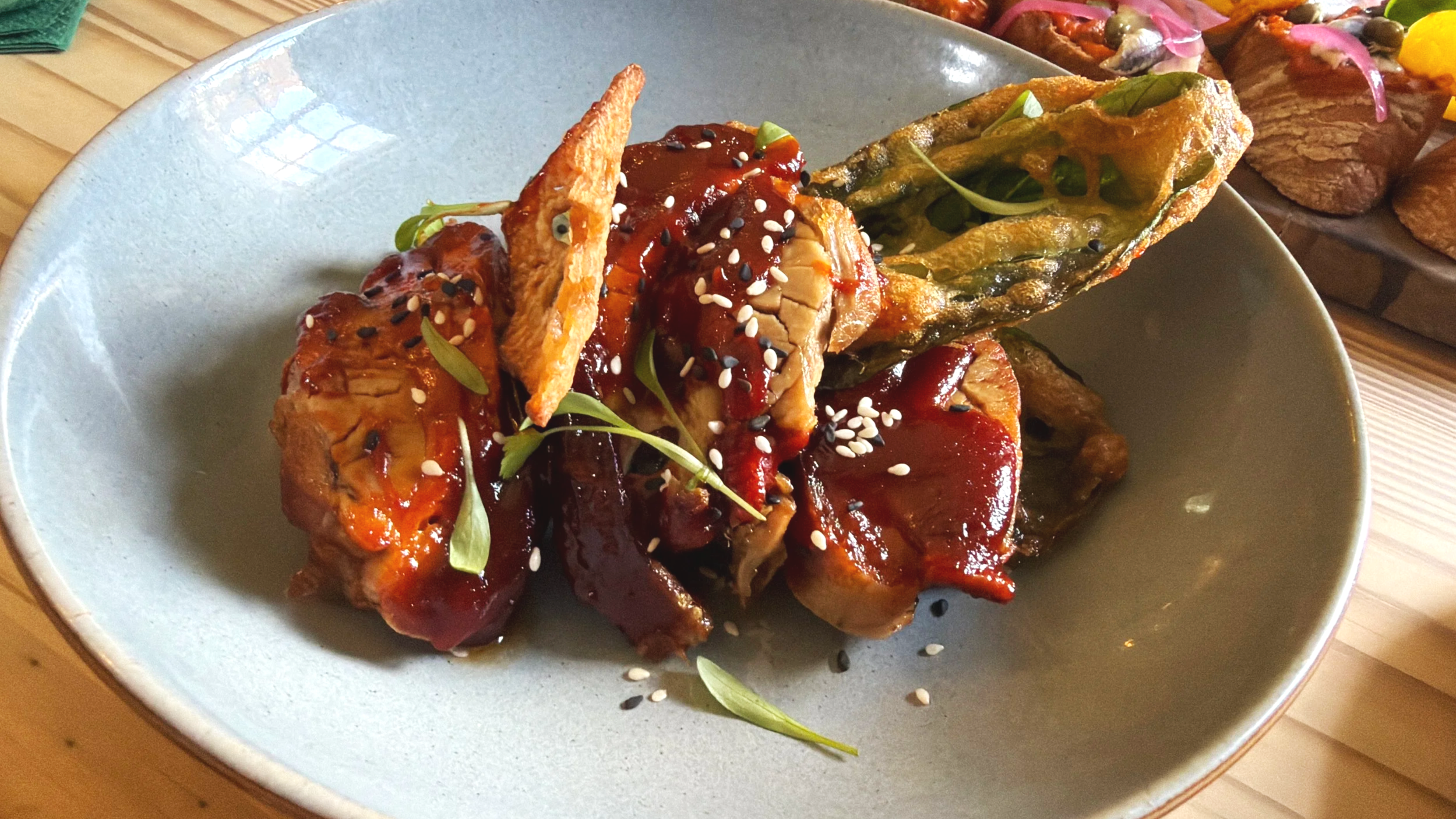 Sushi rolls topped with eel sauce, sprinkled with sesame seeds, served on a light blue plate.
