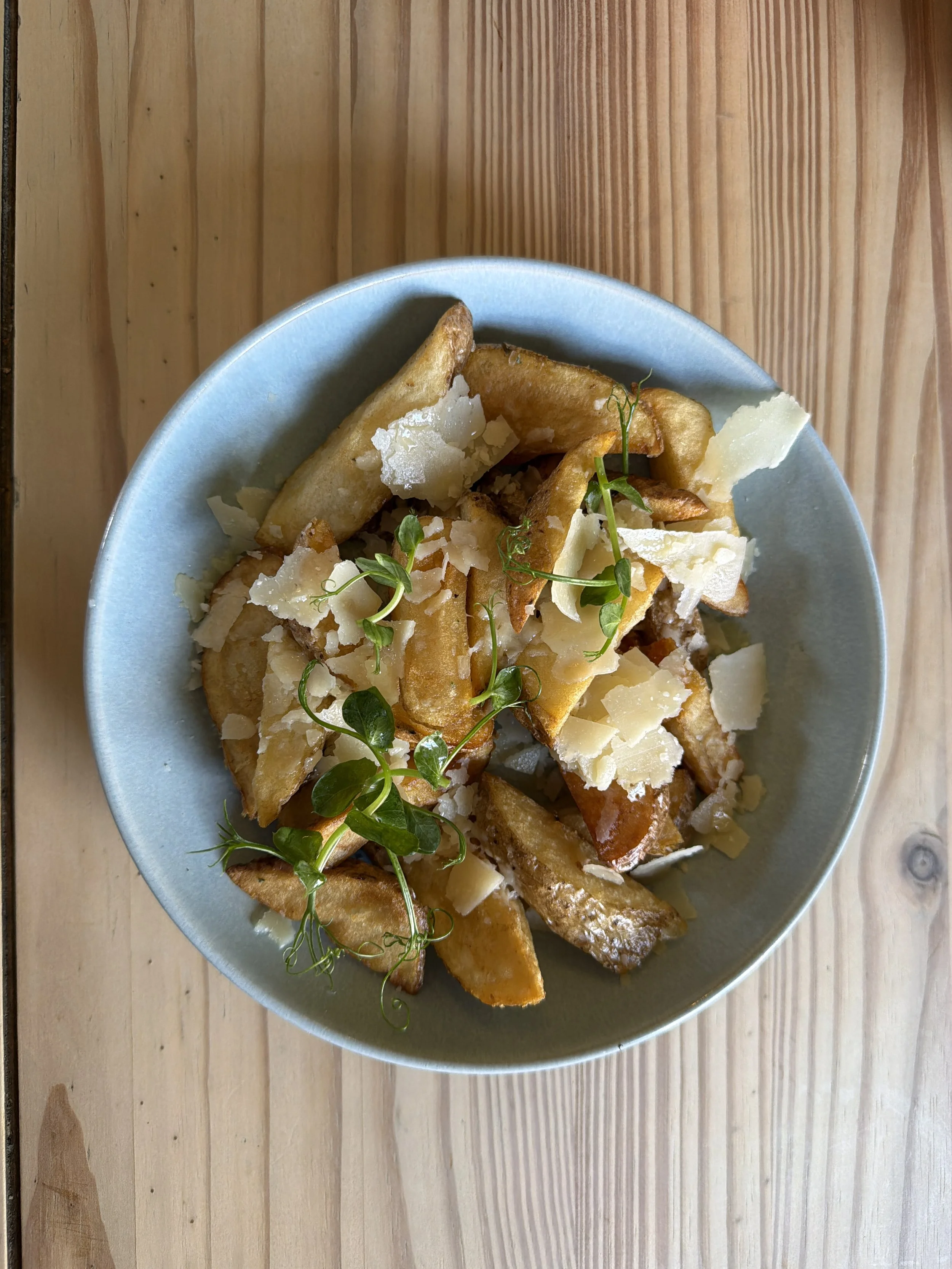 Plate of thick-cut fries topped with grated cheese and garnished with fresh herbs on a wooden surface.