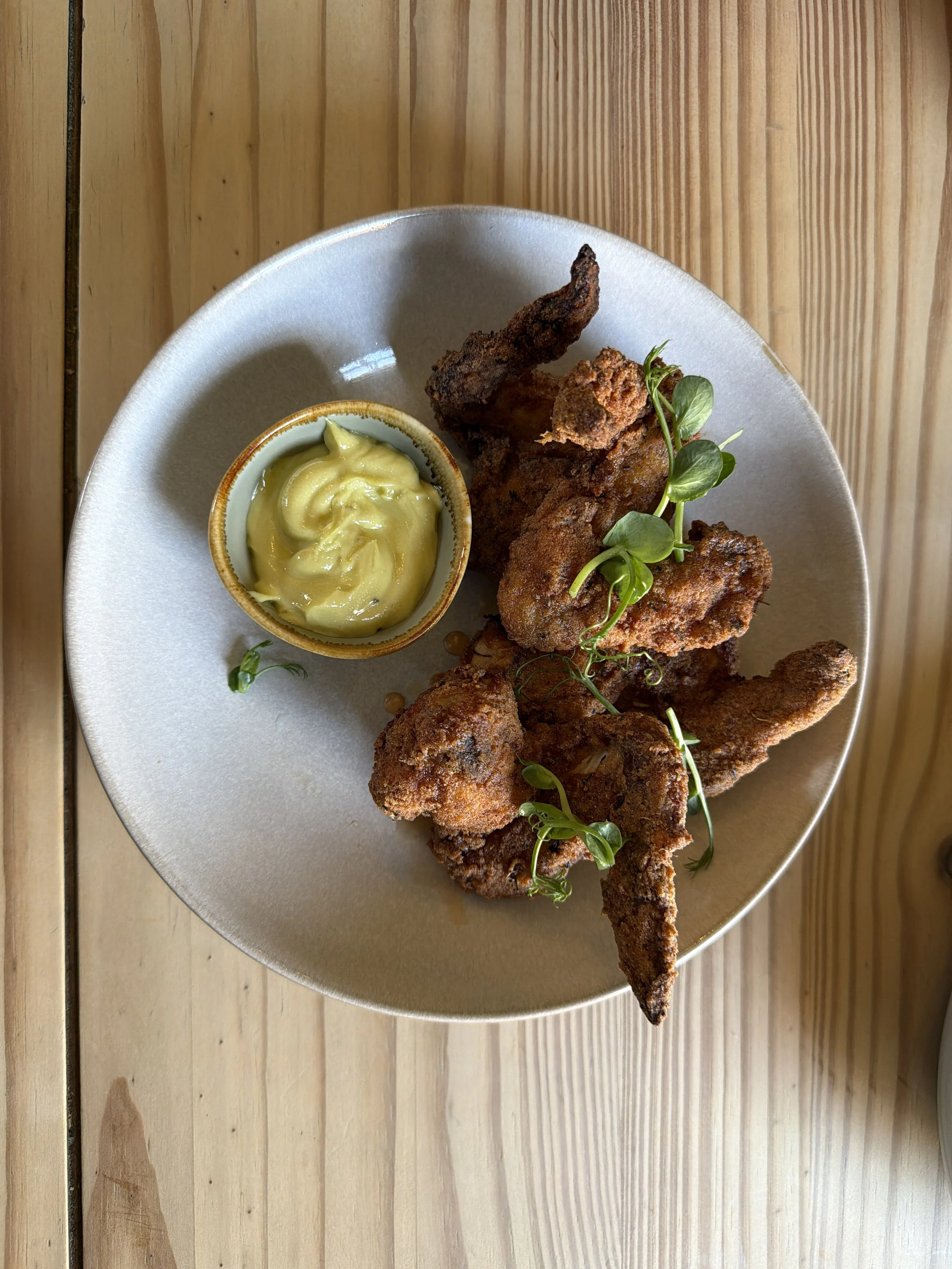 Plate of fried chicken pieces garnished with microgreens and a small bowl of mustard sauce, on a wooden table.