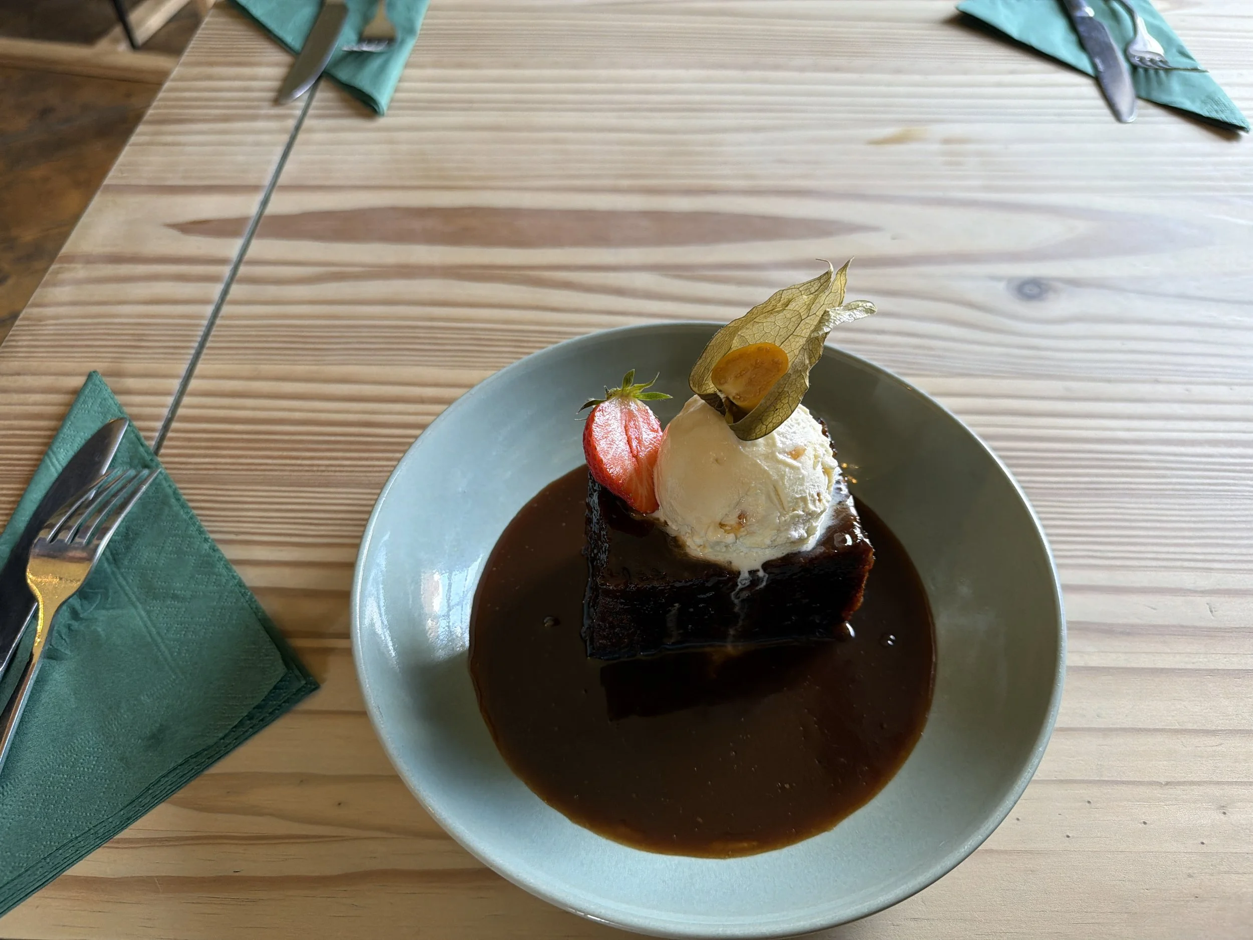 A dessert topped with a scoop of vanilla ice cream, sliced strawberries, and a decorative golden leaf, served in a white bowl with chocolate sauce.