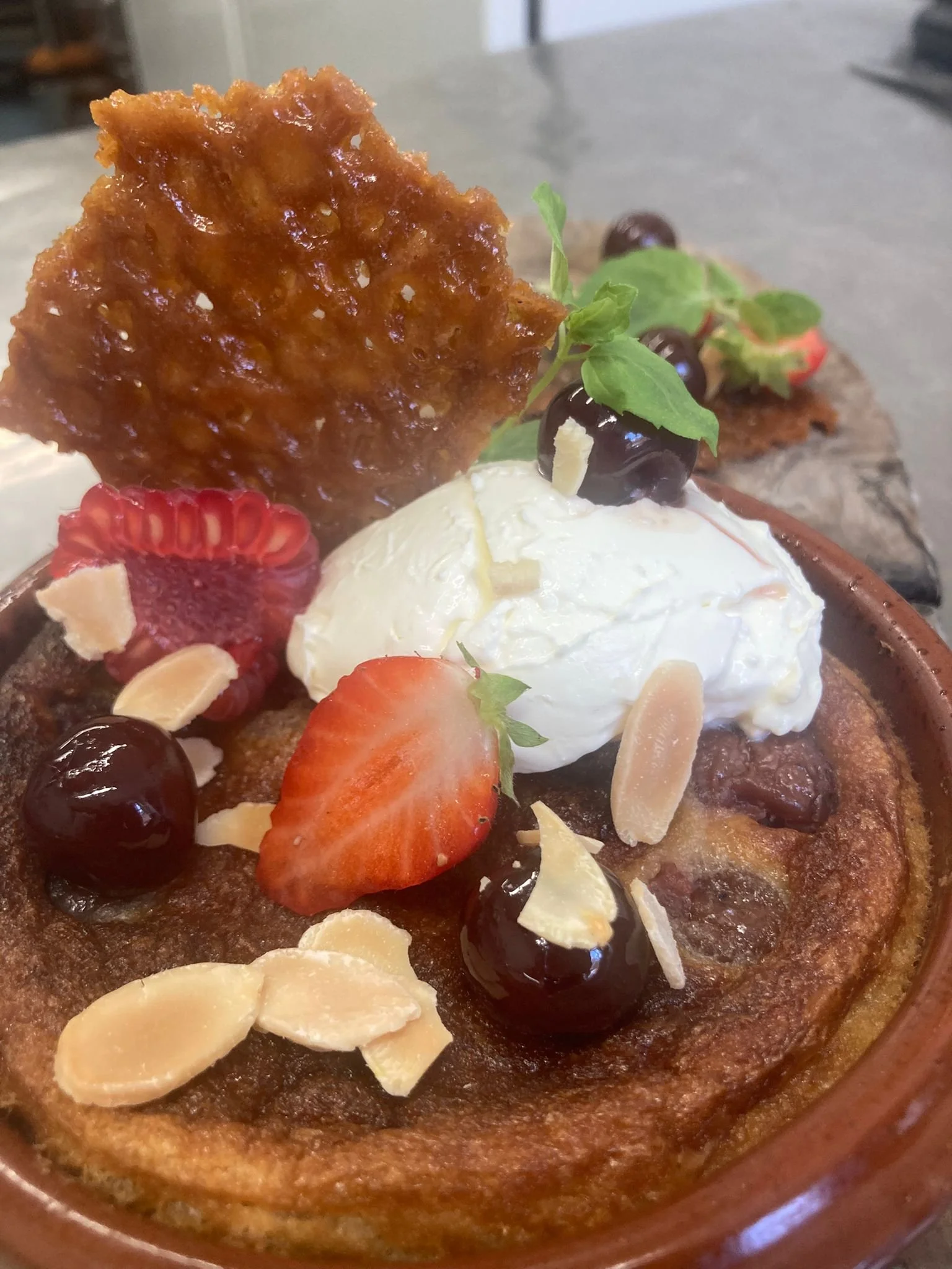 Close-up of a dessert with strawberries, blueberries, sliced almonds, a dollop of whipped cream, and a caramelized tuile cookie on top.