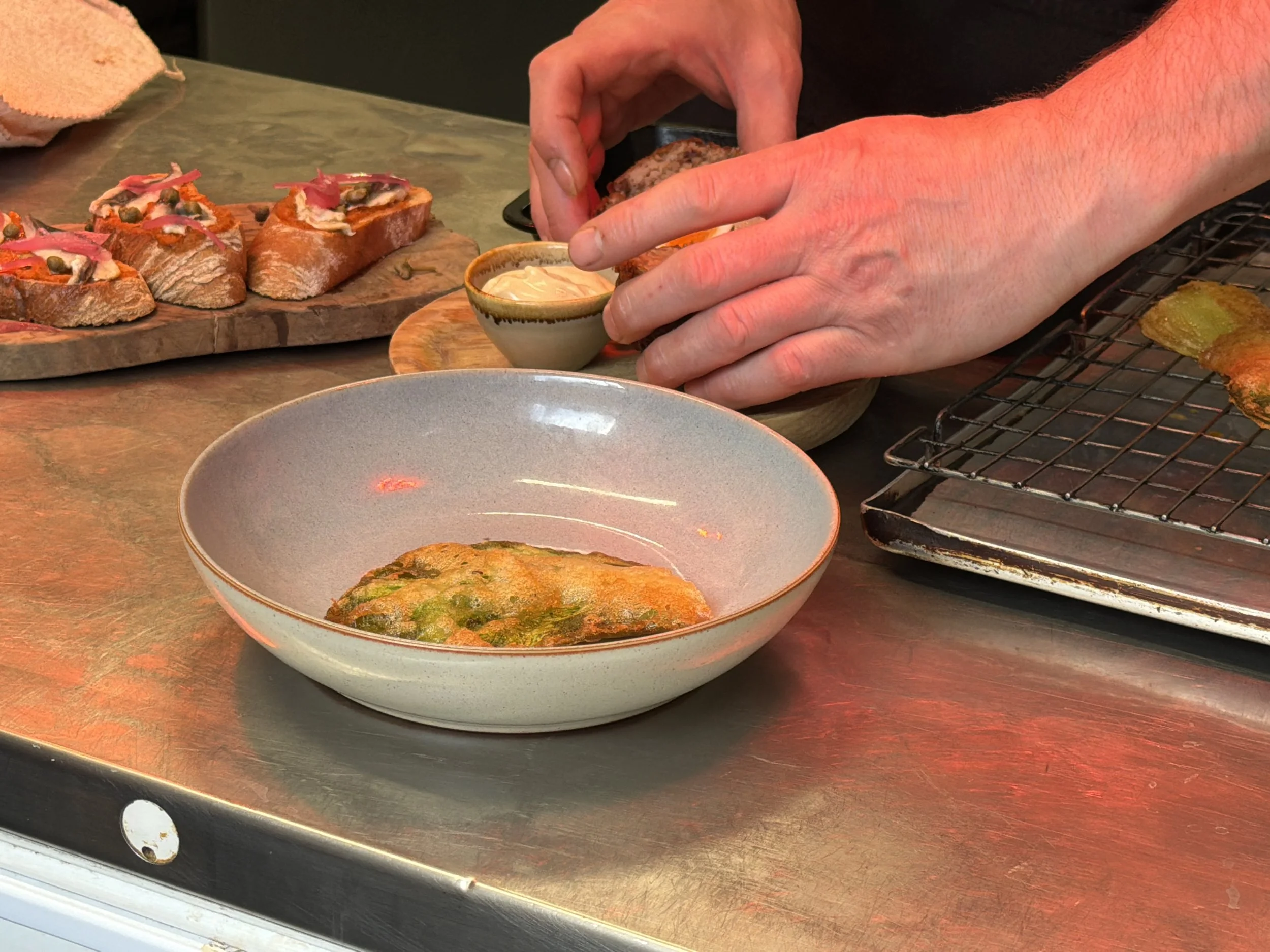 Hands preparing to serve food, with dishes of bread, dip, and fried food on a counter.