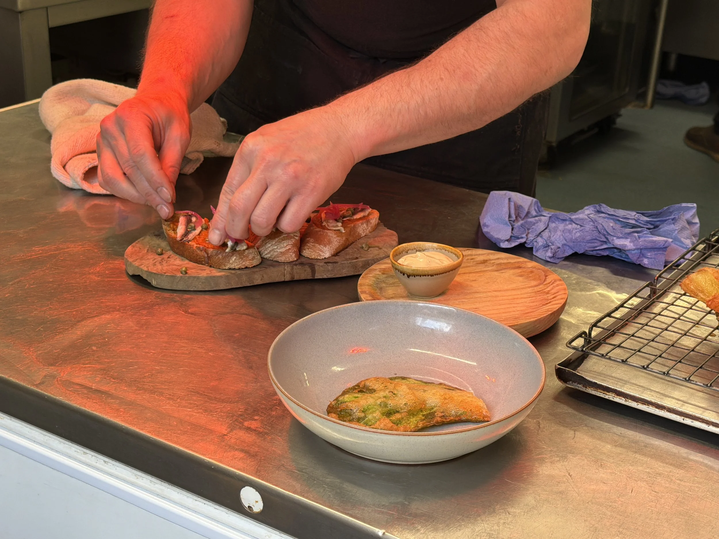 A person preparing open-faced sandwiches with toppings on a kitchen countertop, with various plates and kitchen items around.