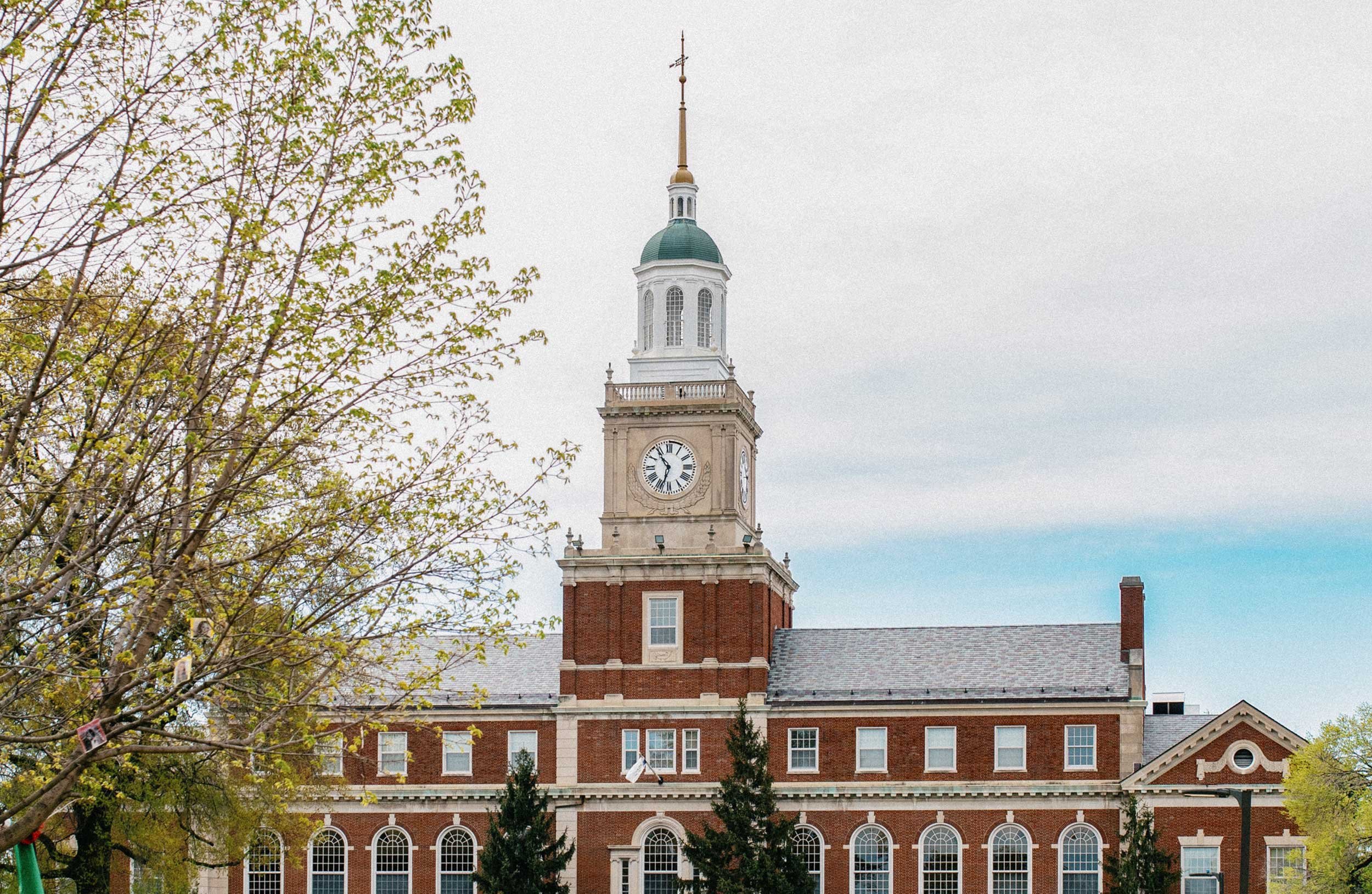 A brick building with a clock tower and a green dome, surrounded by trees, under an overcast sky.