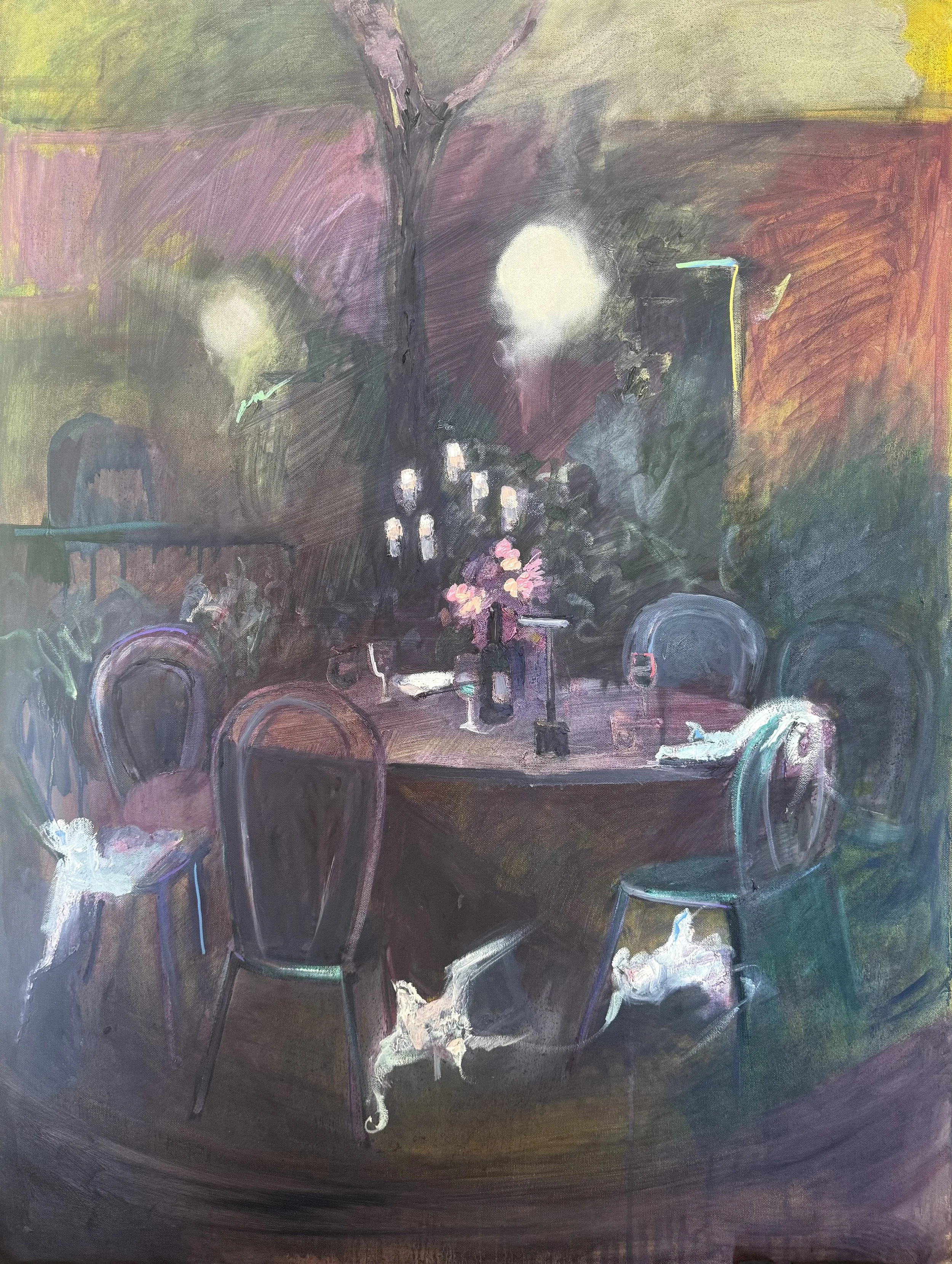 A dimly lit indoor dining scene with a round table set with pink flowers, wine glasses, and a bottle. Surrounding the table are several chairs, with a white cat sitting on one of them and another cat on the floor. The background has dark walls, a large bright light, and abstract artistic elements.