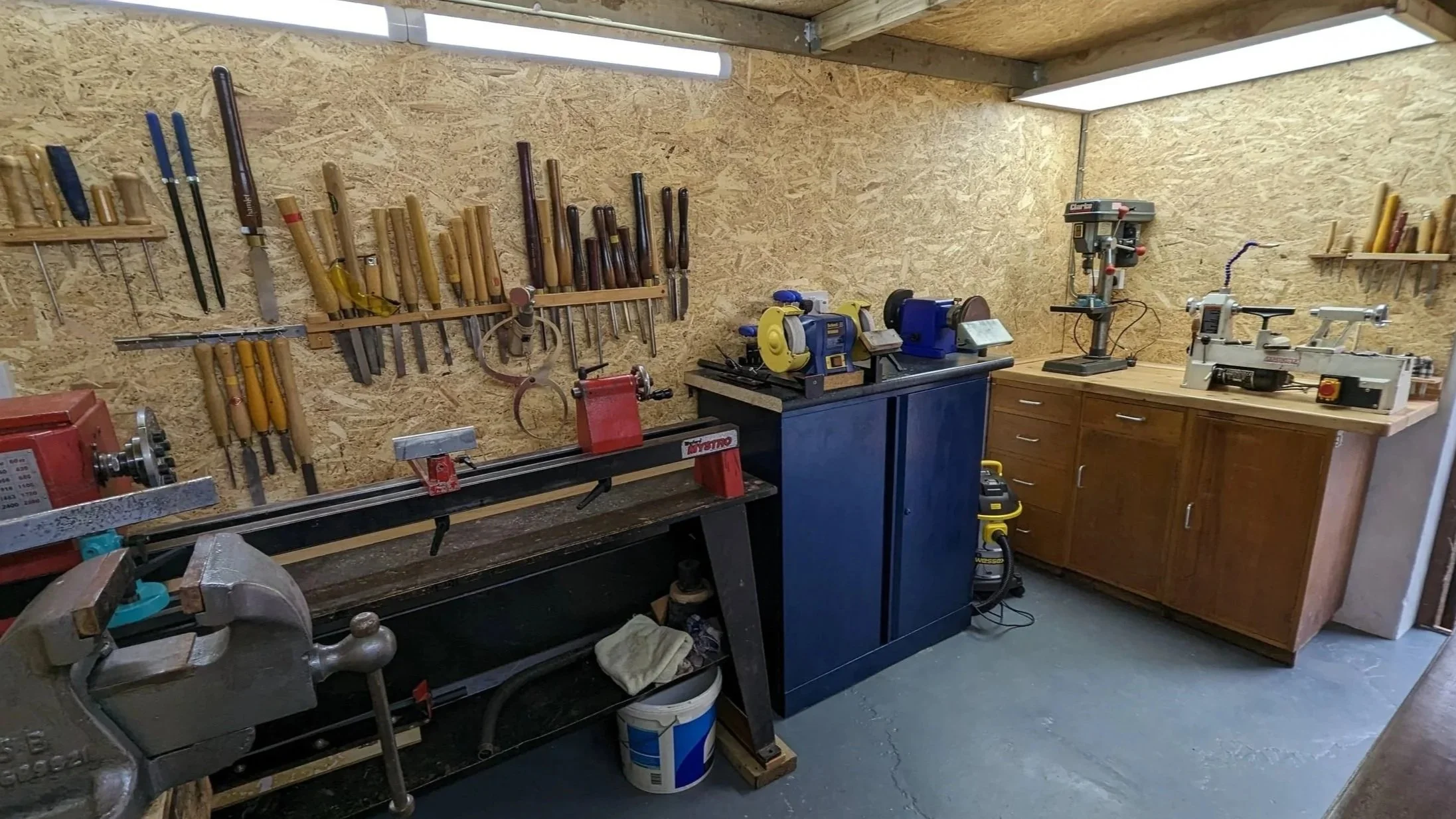 Woodworking workshop with tools on wall, lathe, and workbenches in a well-organized space.