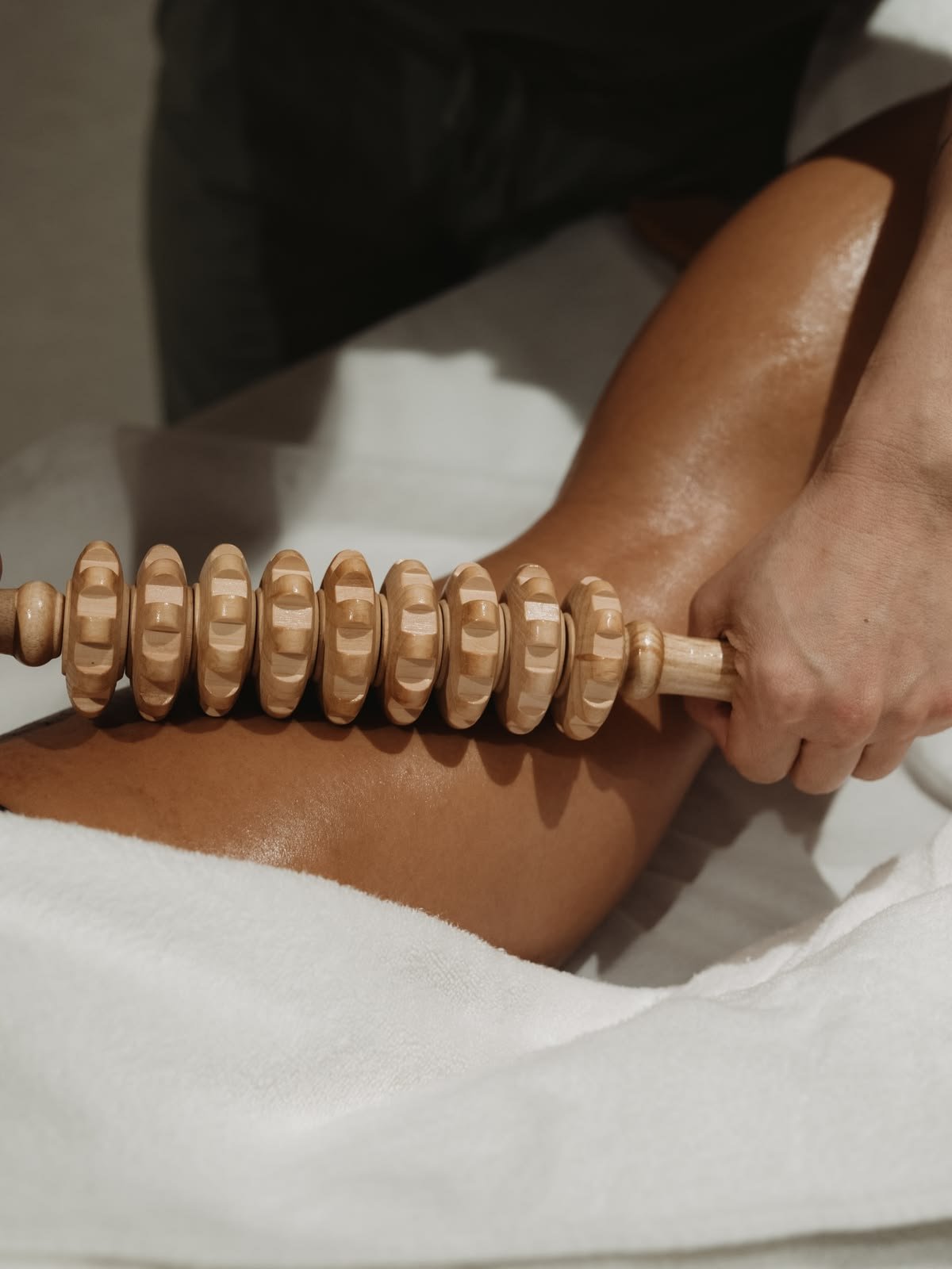 A person receiving a massage using a wooden massage roller on their leg.