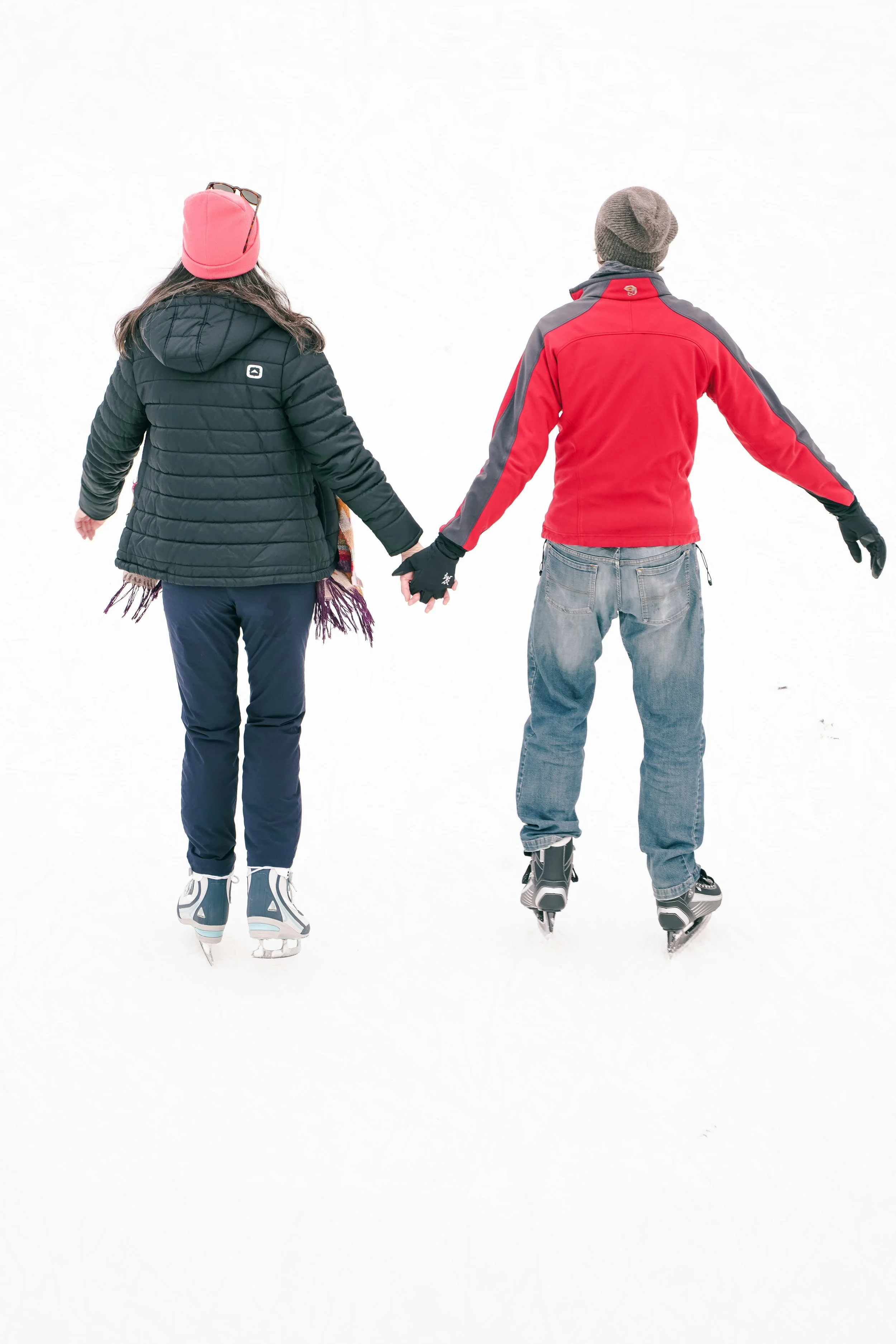 A woman and a man wearing ice skates and winter gear on an outdoor skating rink