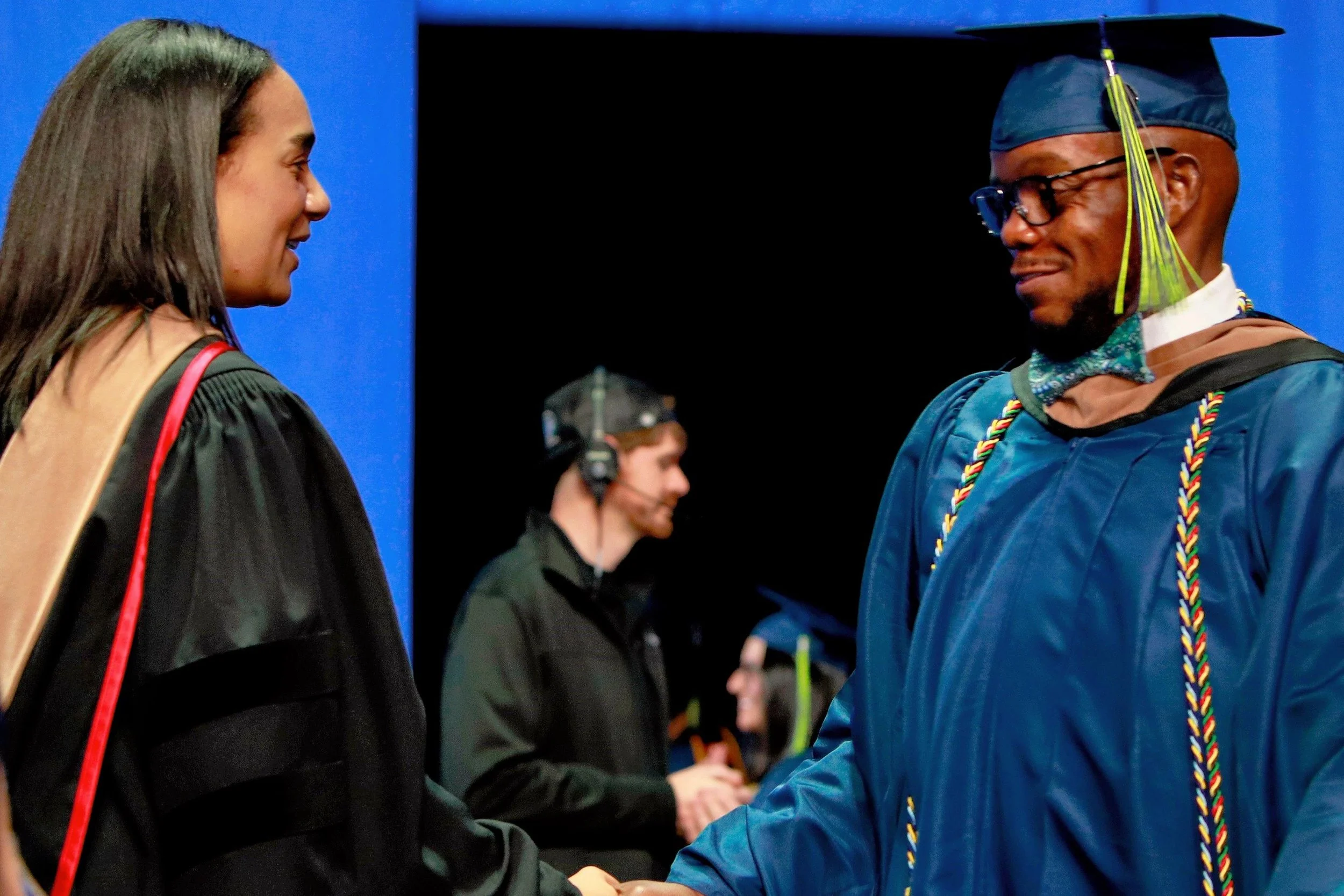 A graduation ceremony where a man in cap and gown is shaking hands with a woman in academic regalia.