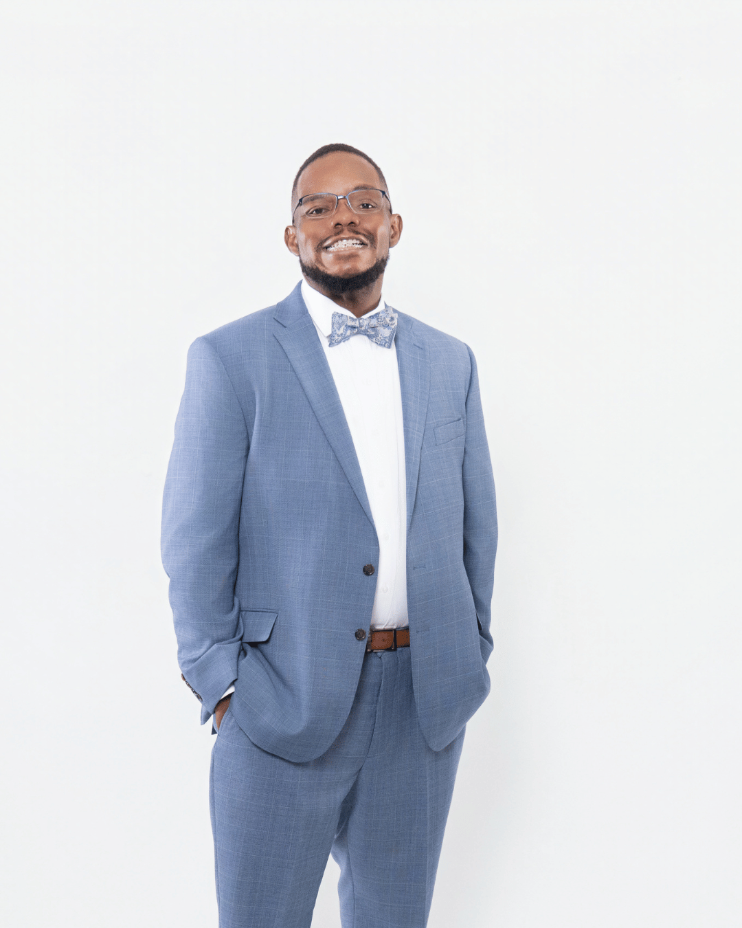Man in a light blue suit with a bow tie standing against a white background.