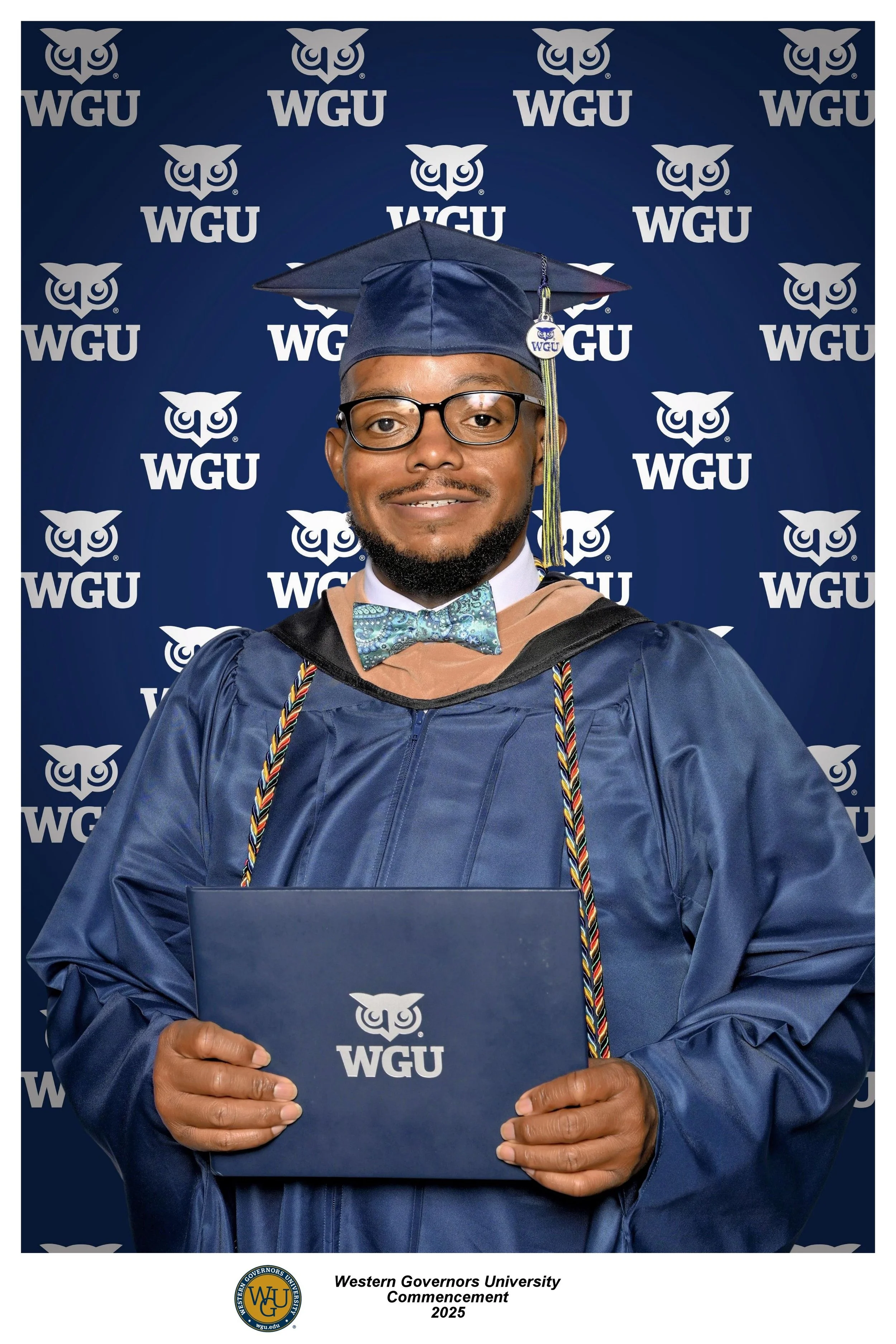 A man wearing a graduation cap and gown, holding a diploma, standing in front of a backdrop with the WGU logo.