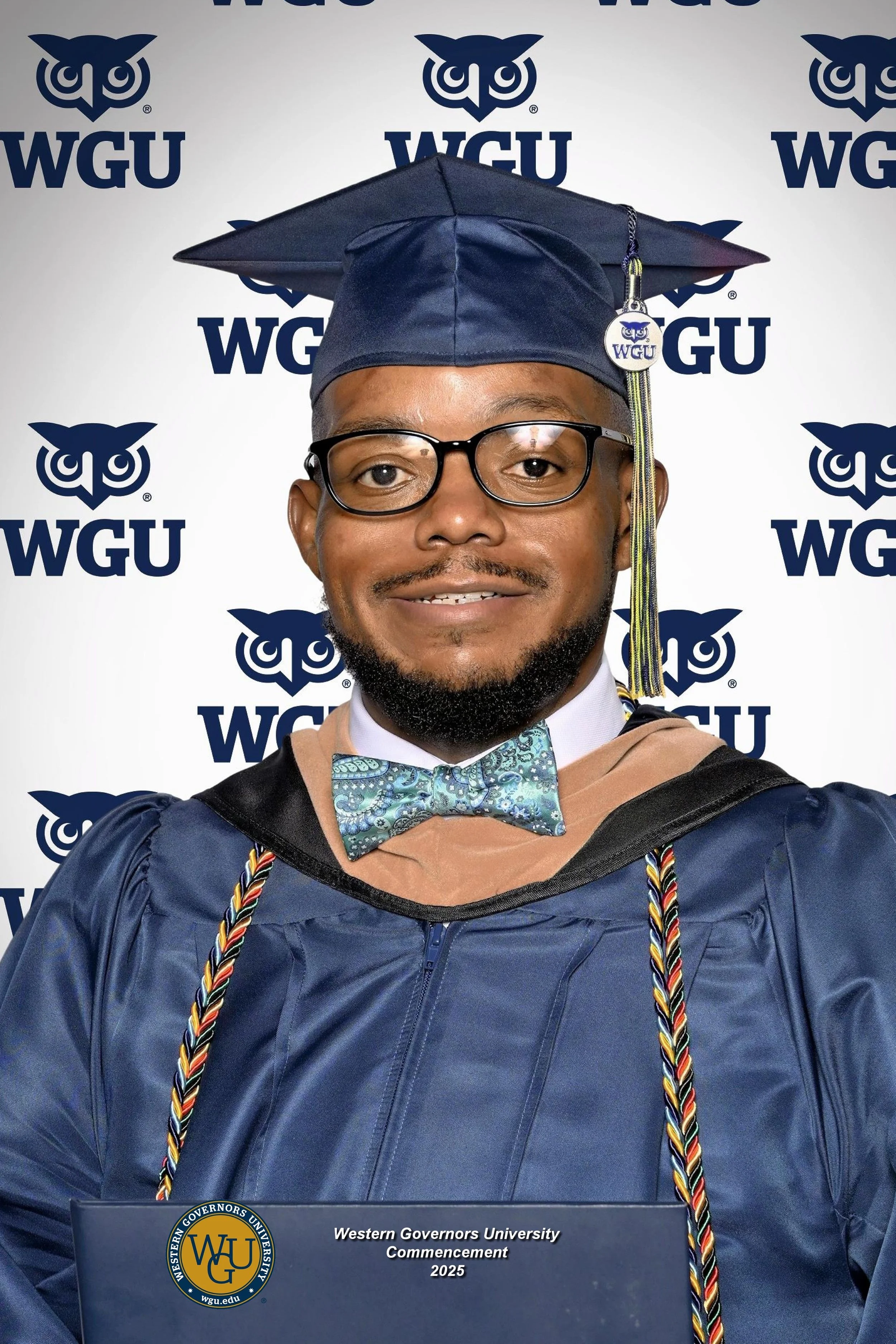 A man in a graduation cap and gown holding a diploma at Western Governors University commencement 2025, standing in front of a WGU branded background.