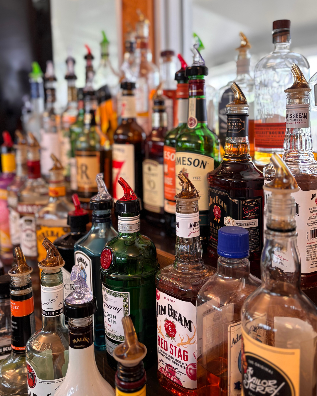 A collection of various liquor bottles, including Jim Beam, Beefeater Gin, and other whiskey and gin bottles, displayed on a bar counter.
