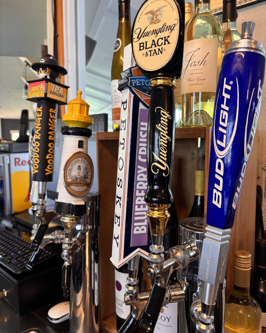 Close-up of beer taps at a bar, featuring brands such as Yuengling, Blue Point, Bud Light, and a lighthouse-shaped tap handle with the label Cheboygan Brewing Company.