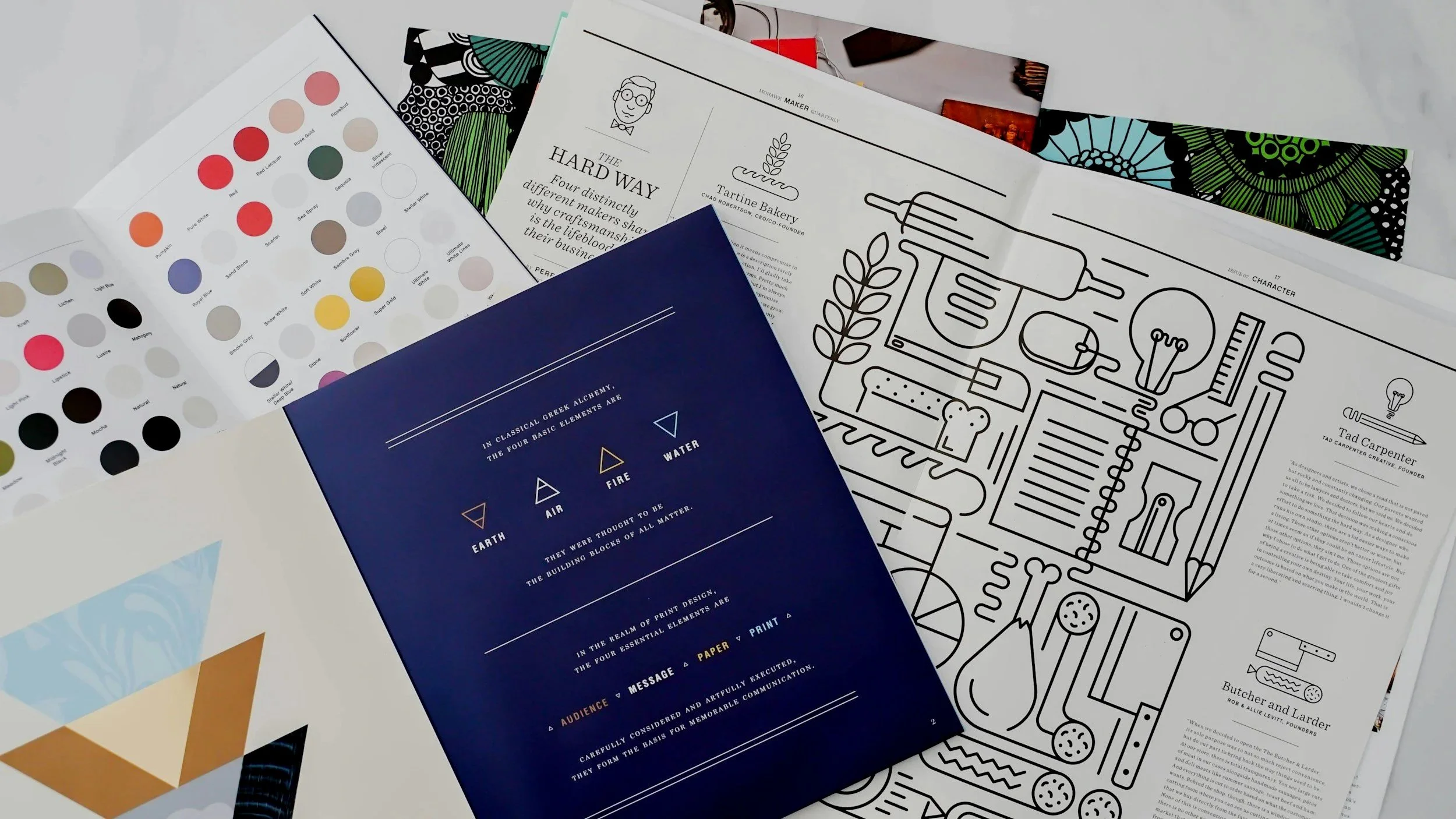 A collection of printed materials, including a color palette, a sheet with line drawings of kitchen utensils, and various articles with text. The items are spread out on a flat surface.