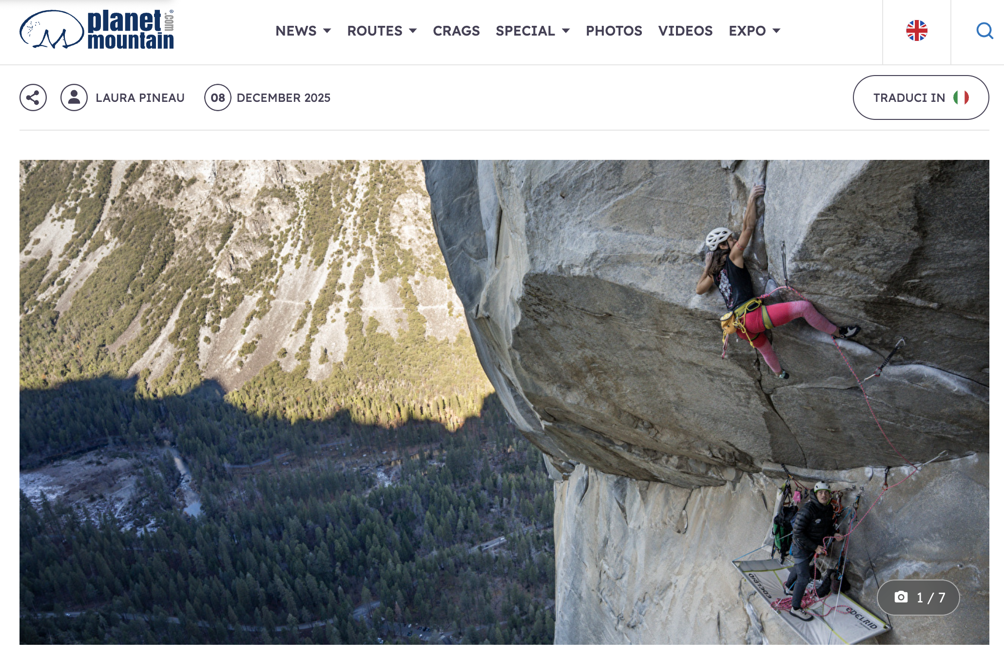 A woman climbing a steep rock wall with a helmet and climbing gear, set against a mountainous landscape.