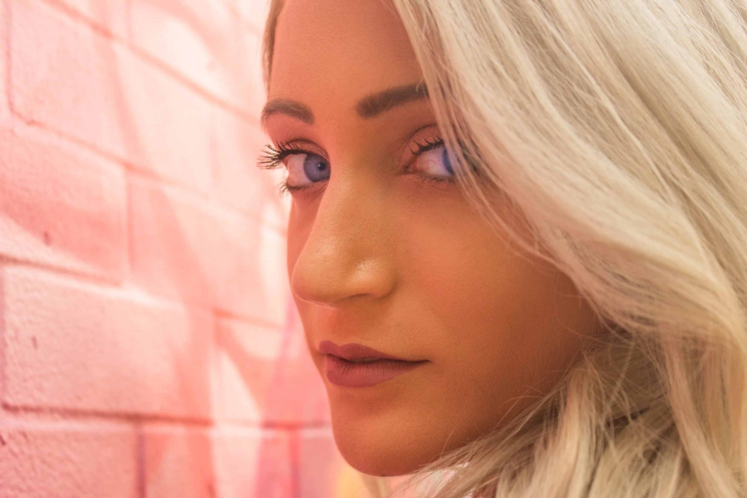 beautiful blonde woman with piercing blue eyes against a pink wall