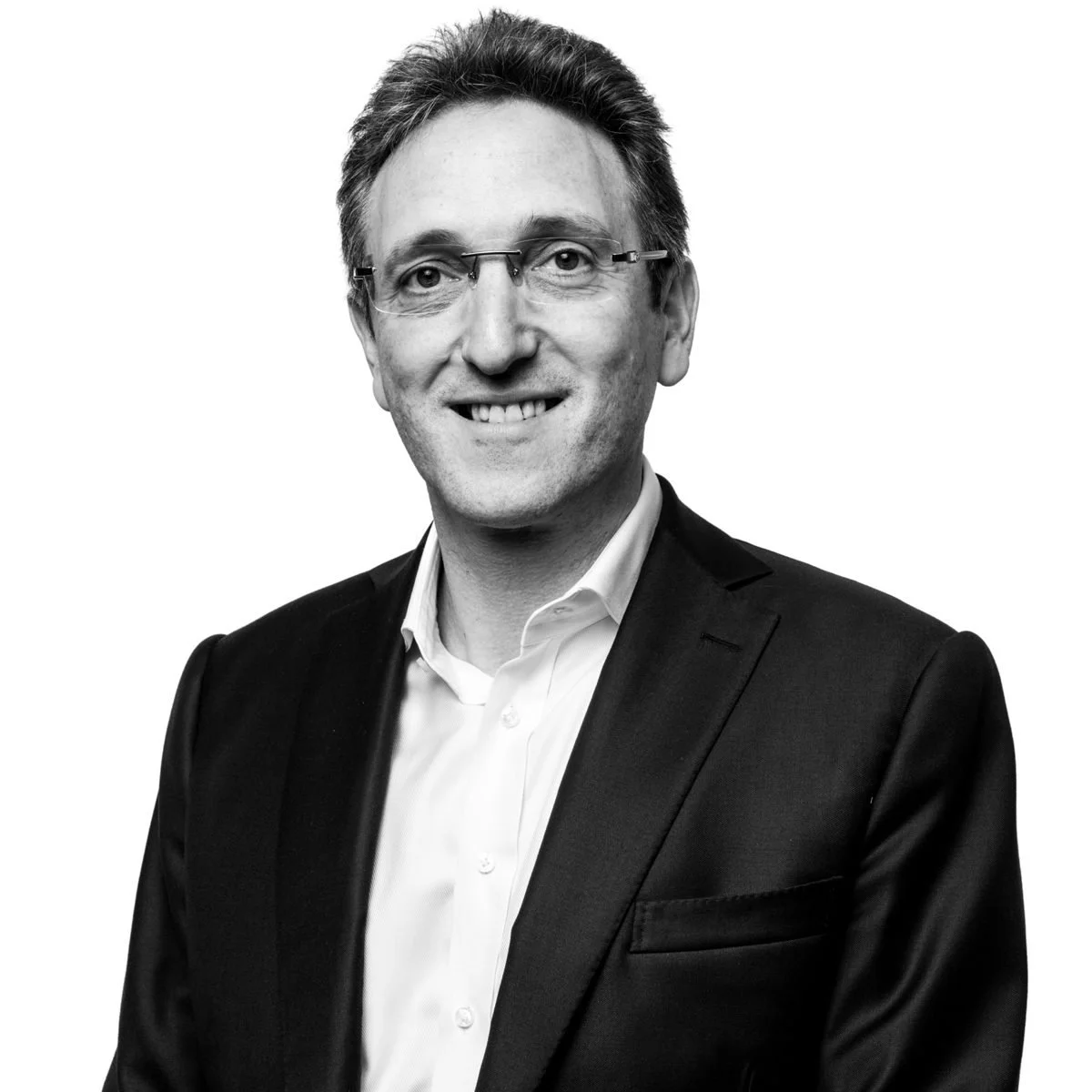 Black and white professional portrait of a man in a suit and glasses, smiling against a plain background.