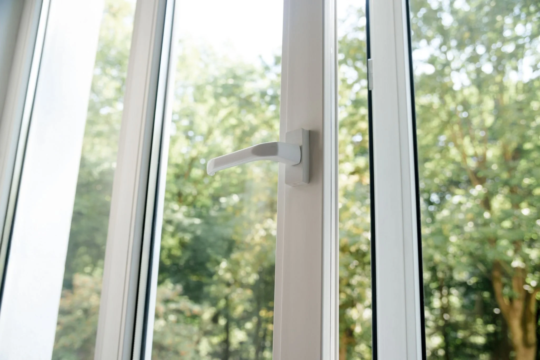 Close-up of a white window latch on a glass door, with trees and greenery outside.