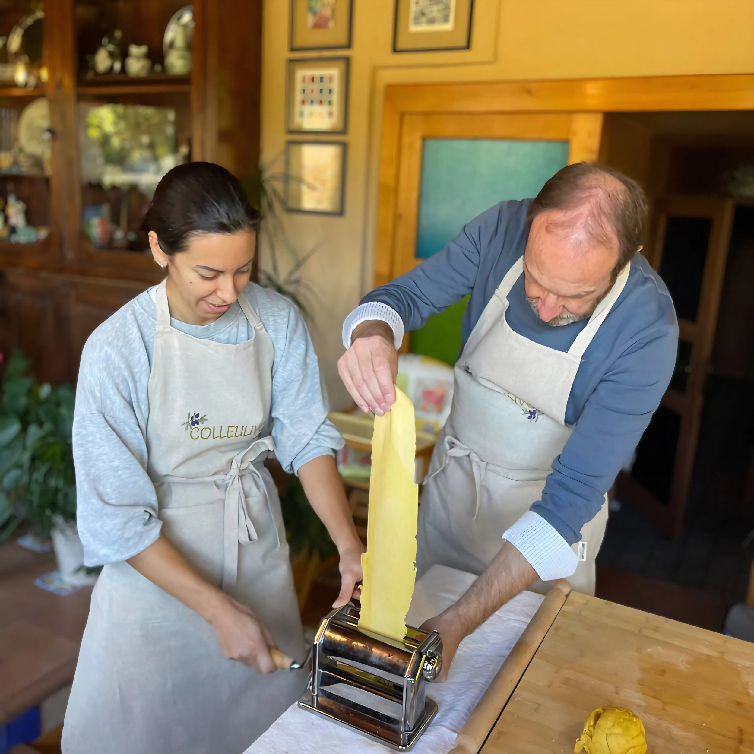 A man and woman making homemade pasta using a pasta machine in a cozy kitchen.
