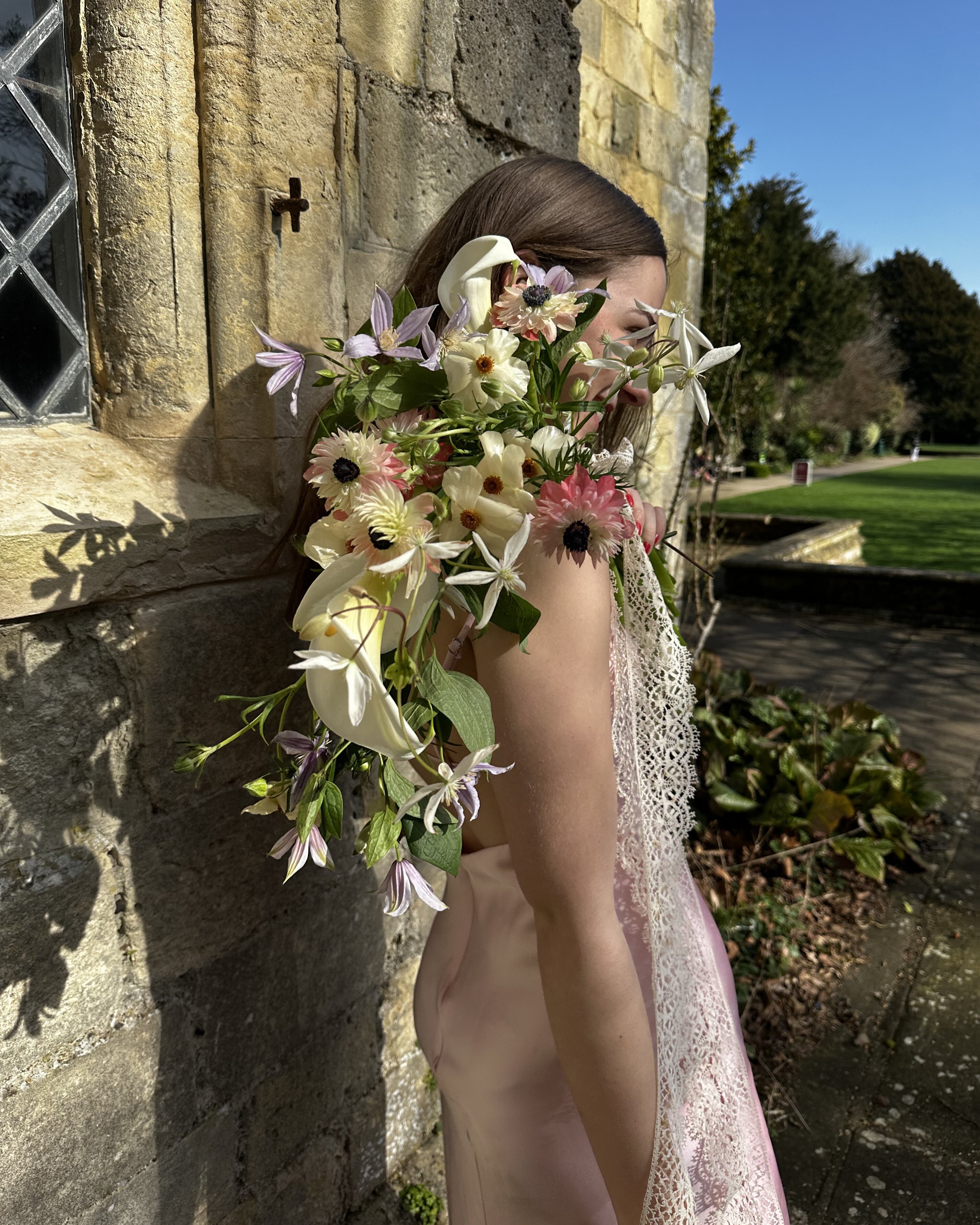 A bride holding a draping bridal bouquet of clematis and calla lilies outside of Lewes registry office