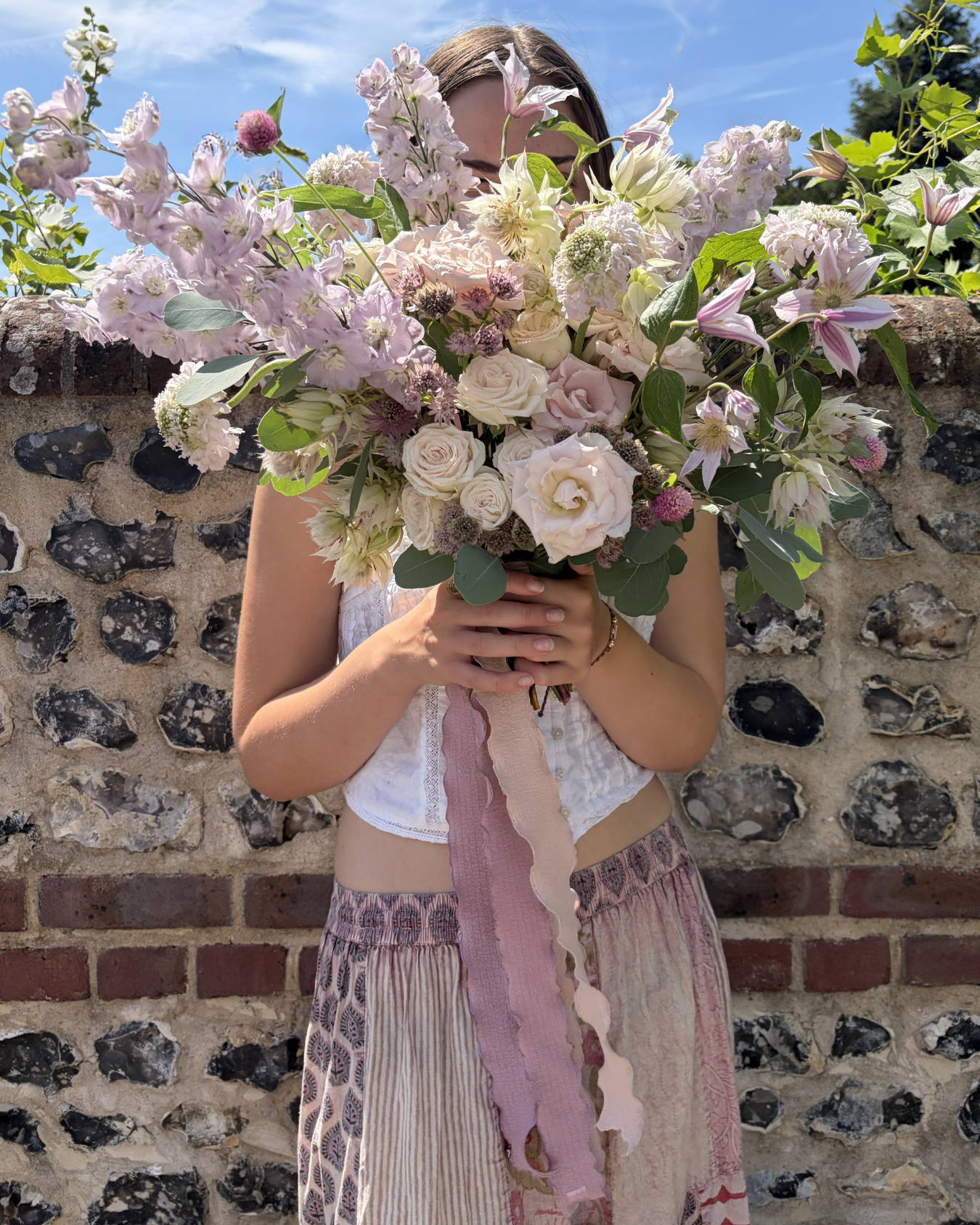 A large bridal bouquet of pastel coloured flowers in front of a flint wall in Lewes, East Sussex