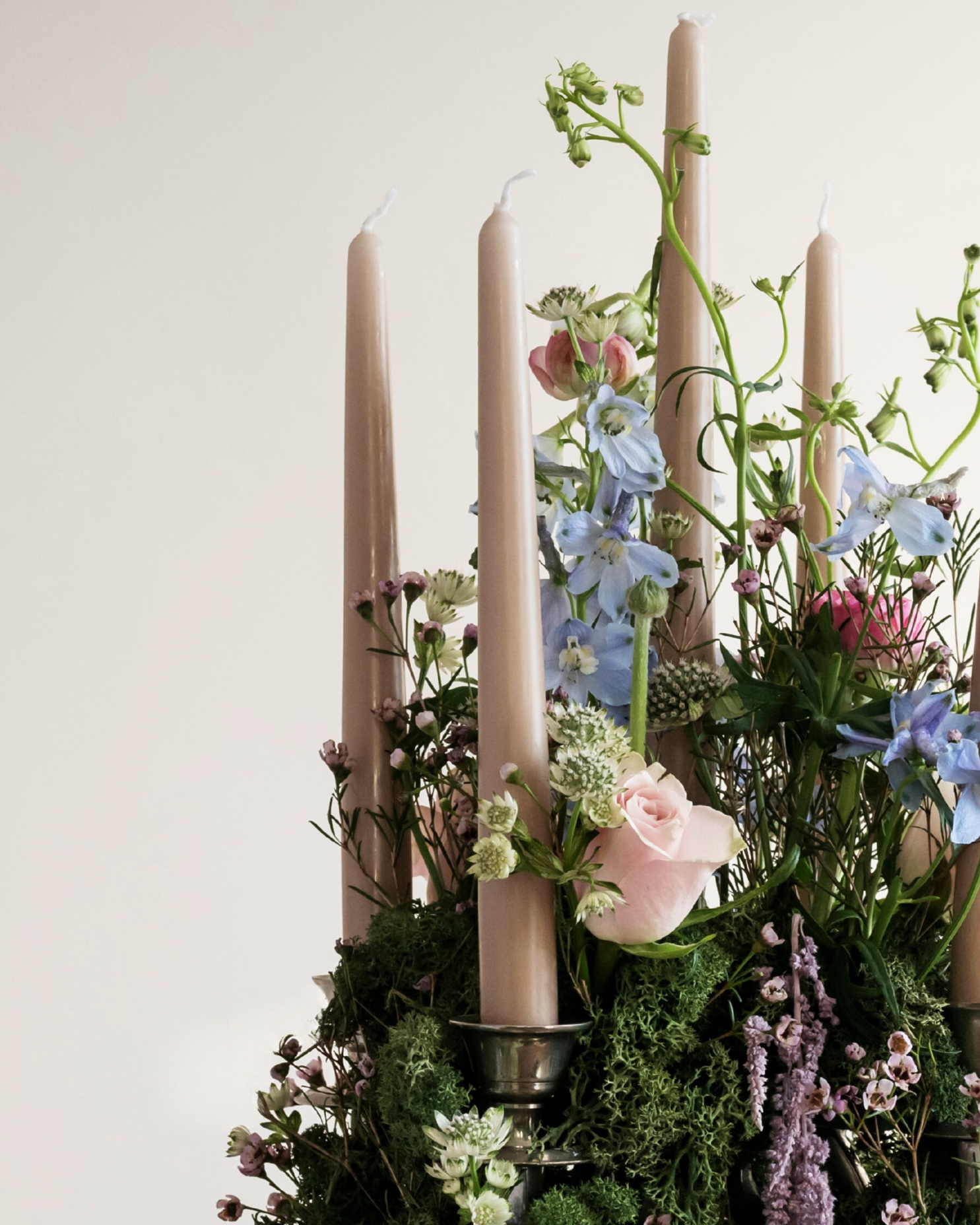 A floral arrangement on a silver candelabra with pink candles, pink roses, and blue and white flowers with moss to create a warm atmoshere for an event