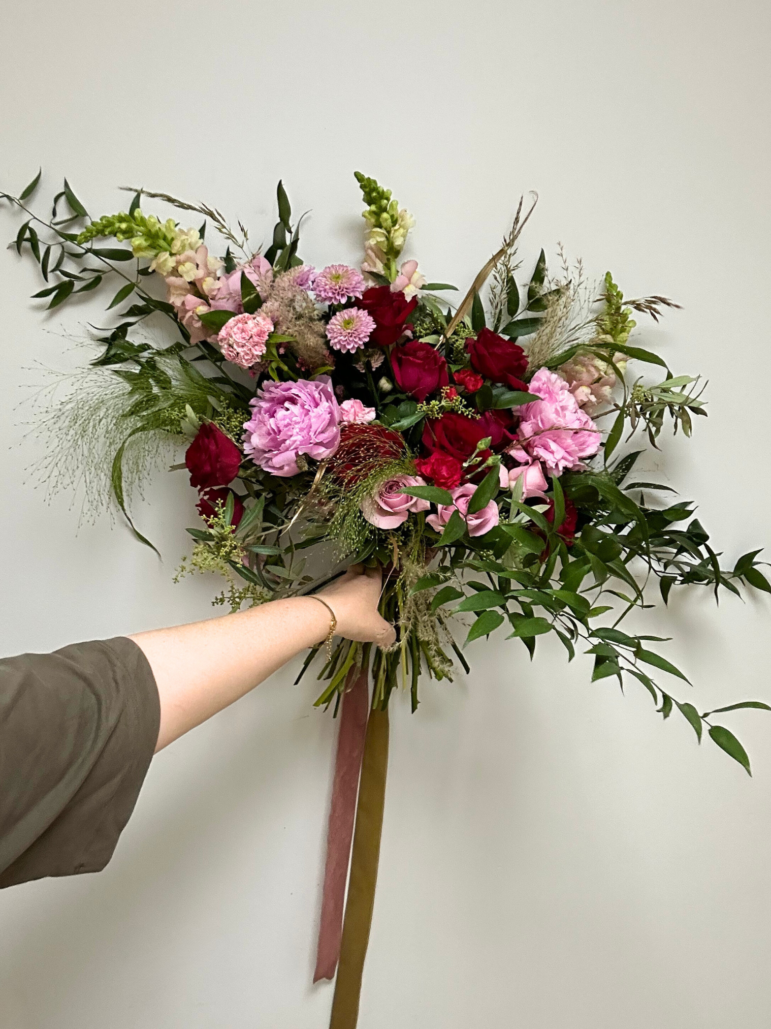A florist holding a large wedding bouquet of pink peonies, red roses, and eucalyptus 