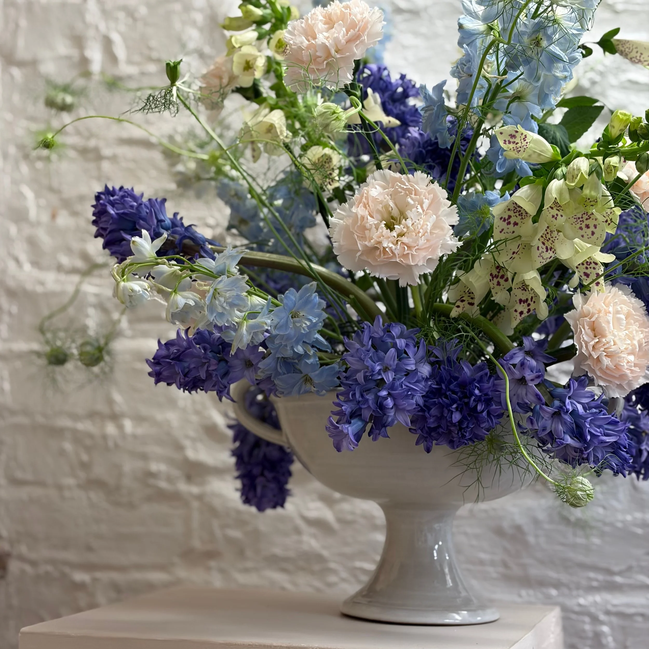 A stoneware pedestal vase filled with blue pink and yellow flowers for an event in Sussex